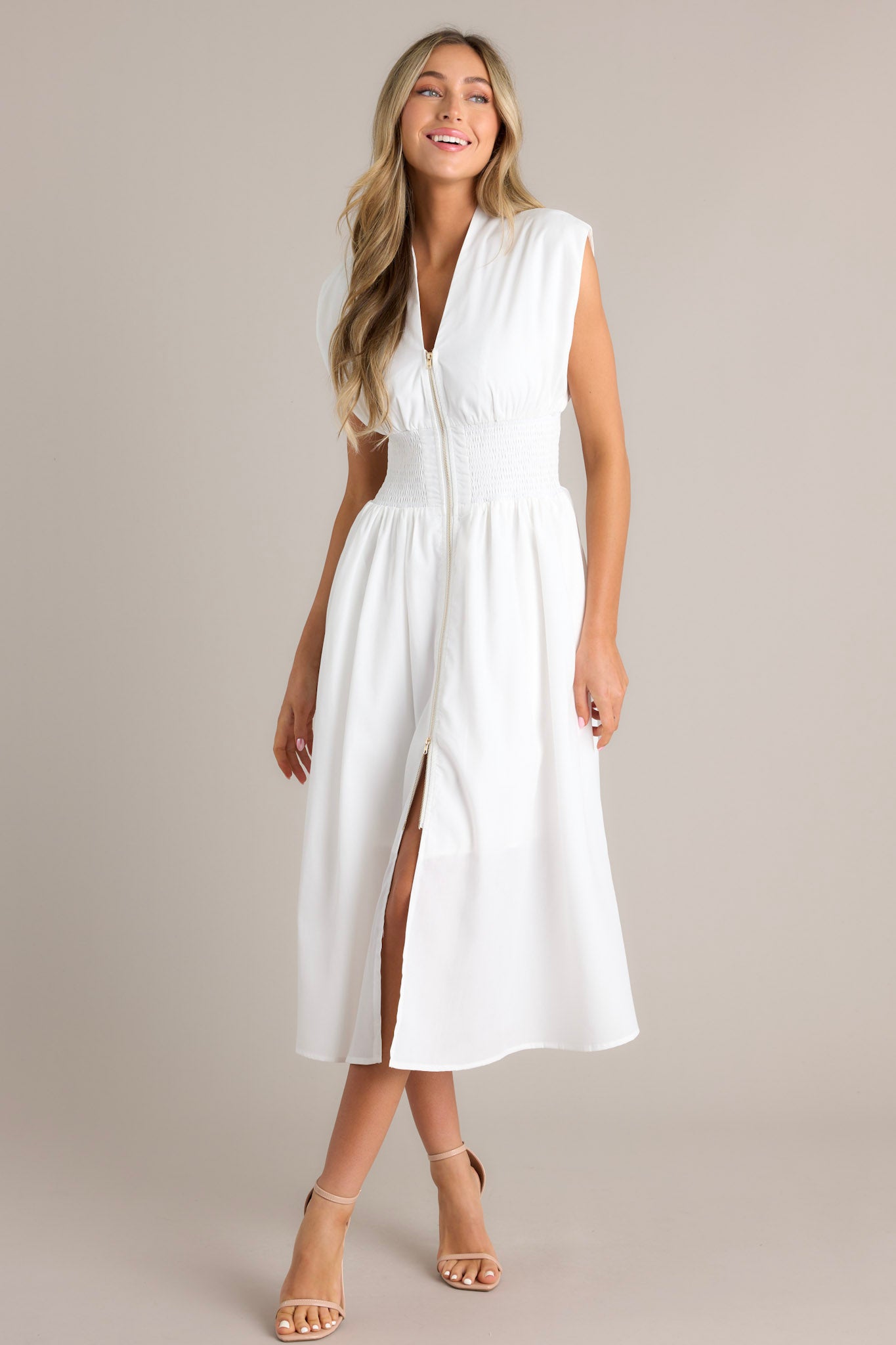 White dress with a V-neckline, cap sleeves, a zippered front, and a cinched waist with shirred detailing, featuring a flowing midi-length skirt with a front slit.