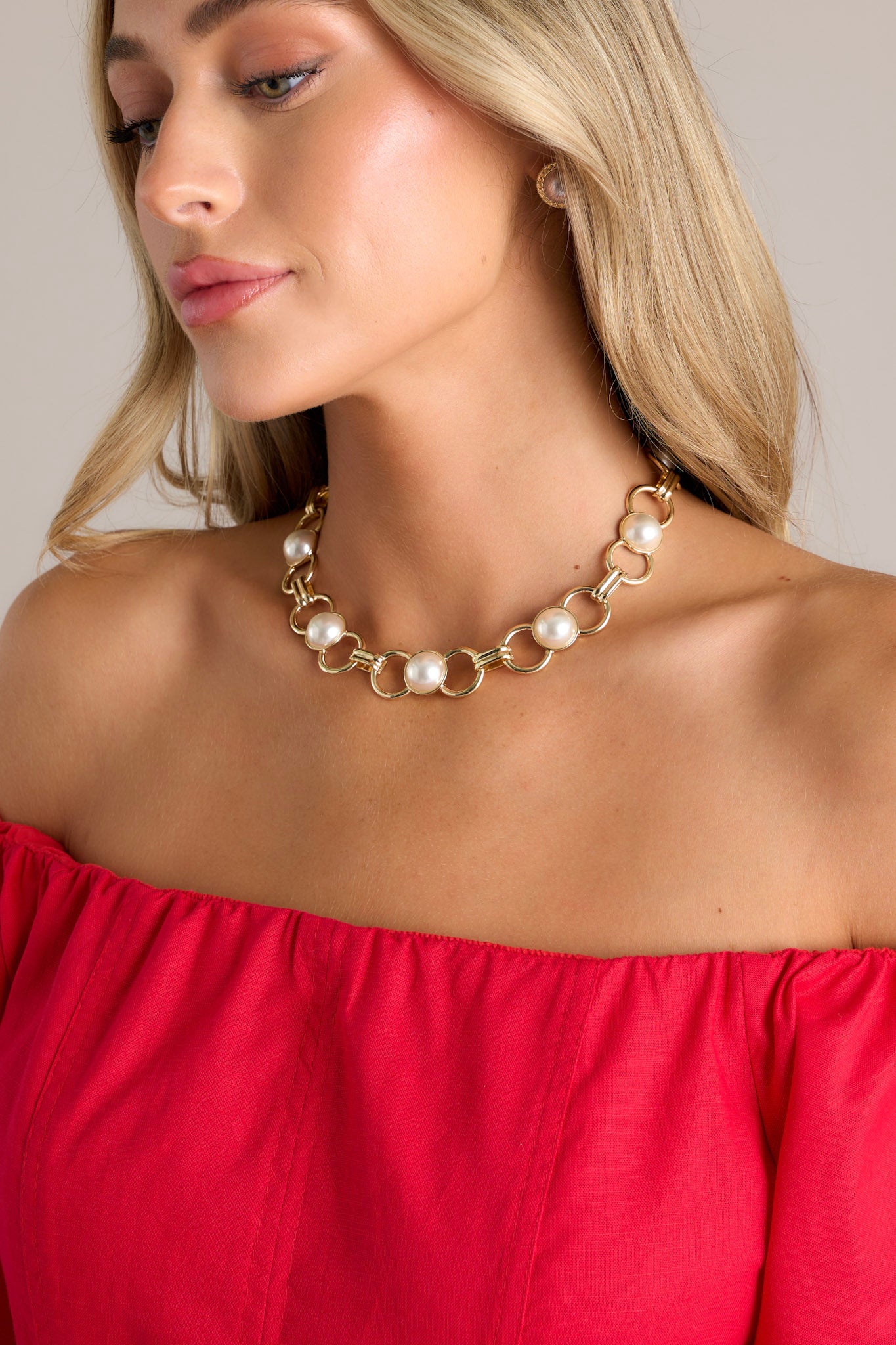 This gold necklace features gold hardware, chunky gold chain links, embedded pearl accents, and a lobster claw closure.
