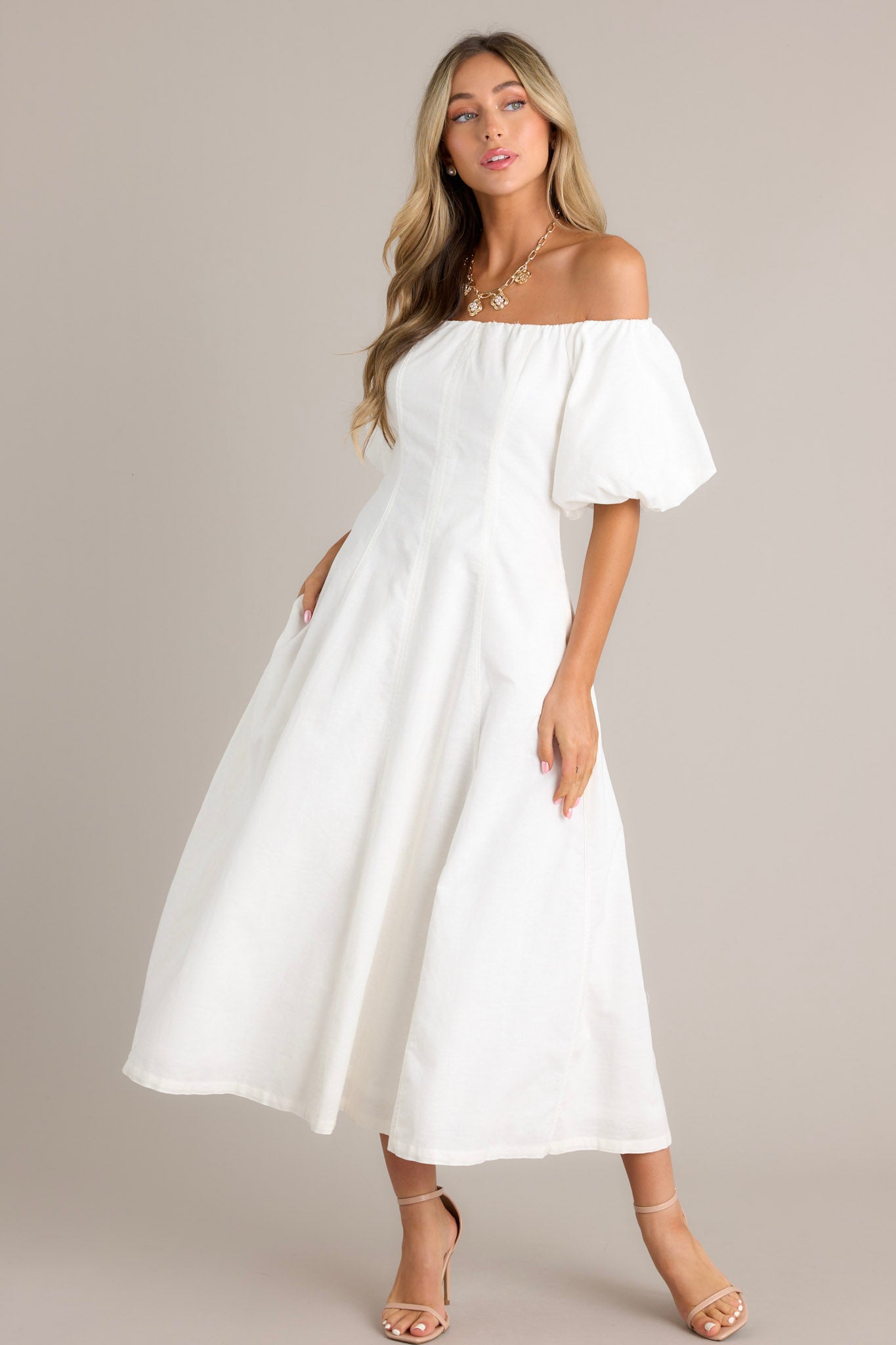 Angled Front view of an elegant off-the-shoulder white dress with puffed sleeves, a fitted bodice, and a flowing ankle-length skirt, featuring side pockets for added practicality.