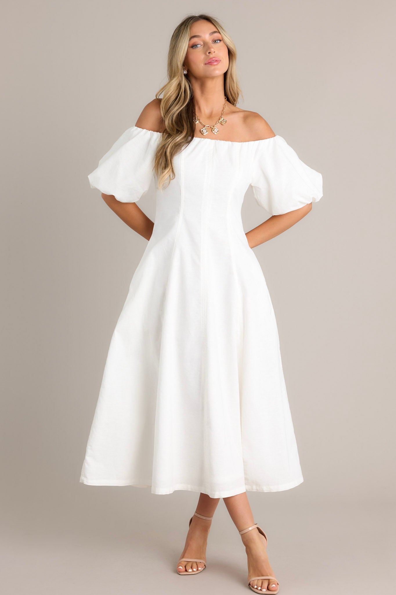 Full body view of an elegant off-the-shoulder white dress with voluminous puffed sleeves, a fitted bodice, and a flowing ankle-length skirt, showcasing a chic and sophisticated design.