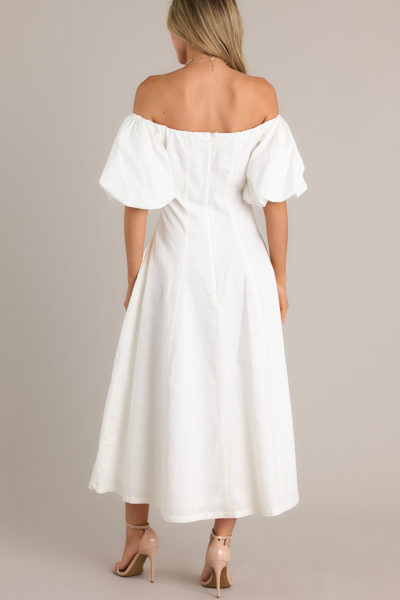 Back view of an elegant off-the-shoulder white dress with voluminous puffed sleeves, a fitted bodice, and a flowing ankle-length skirt, showcasing a chic and sophisticated design.