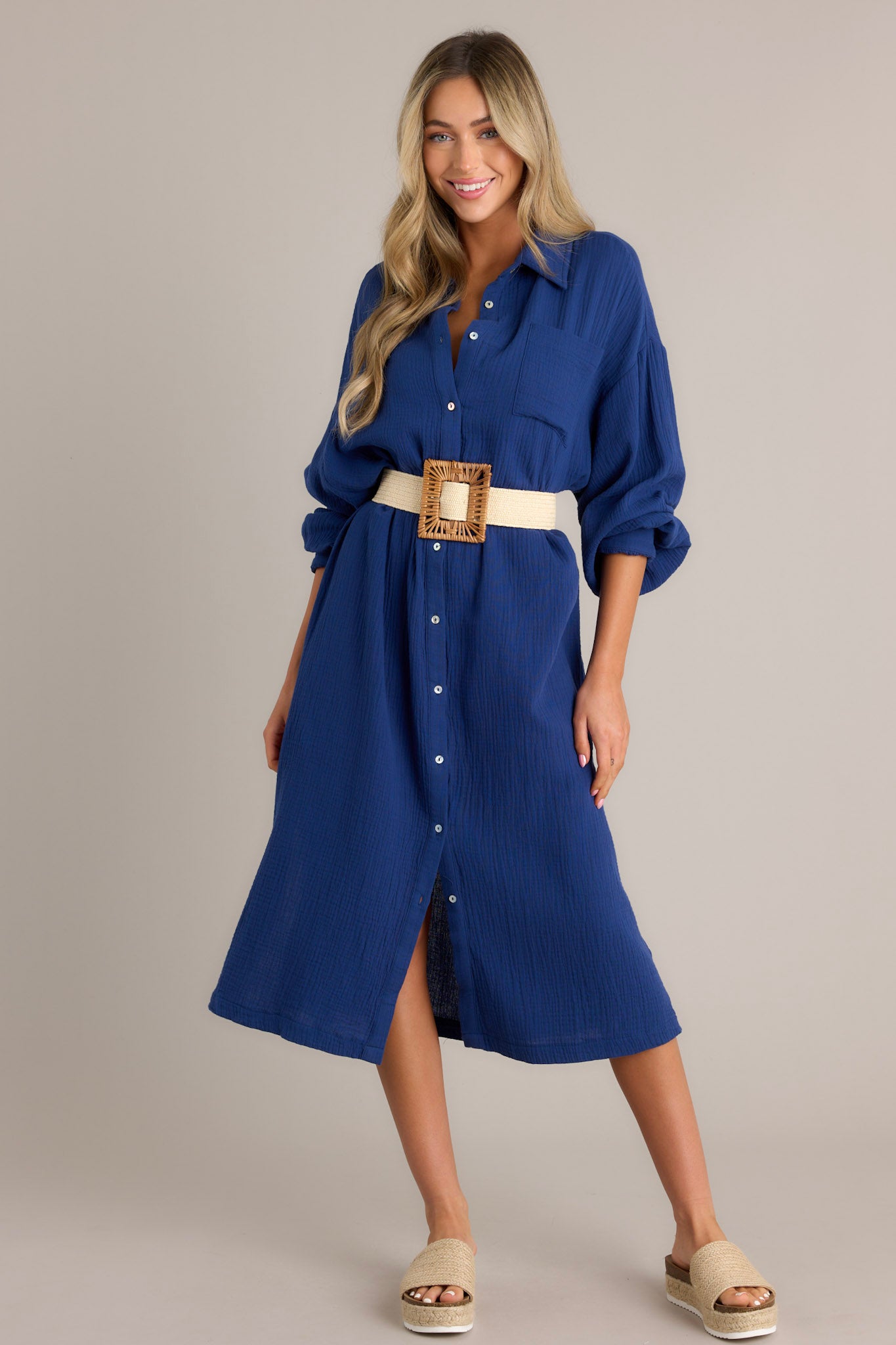 This Navy Gauze Midi Dress features a collared neckline, functional buttons down the front, a front pocket on the left side of the bust, long sleeves with a cuff secured by a functional button, and two slits up the bottom hemline ending just below the knee.