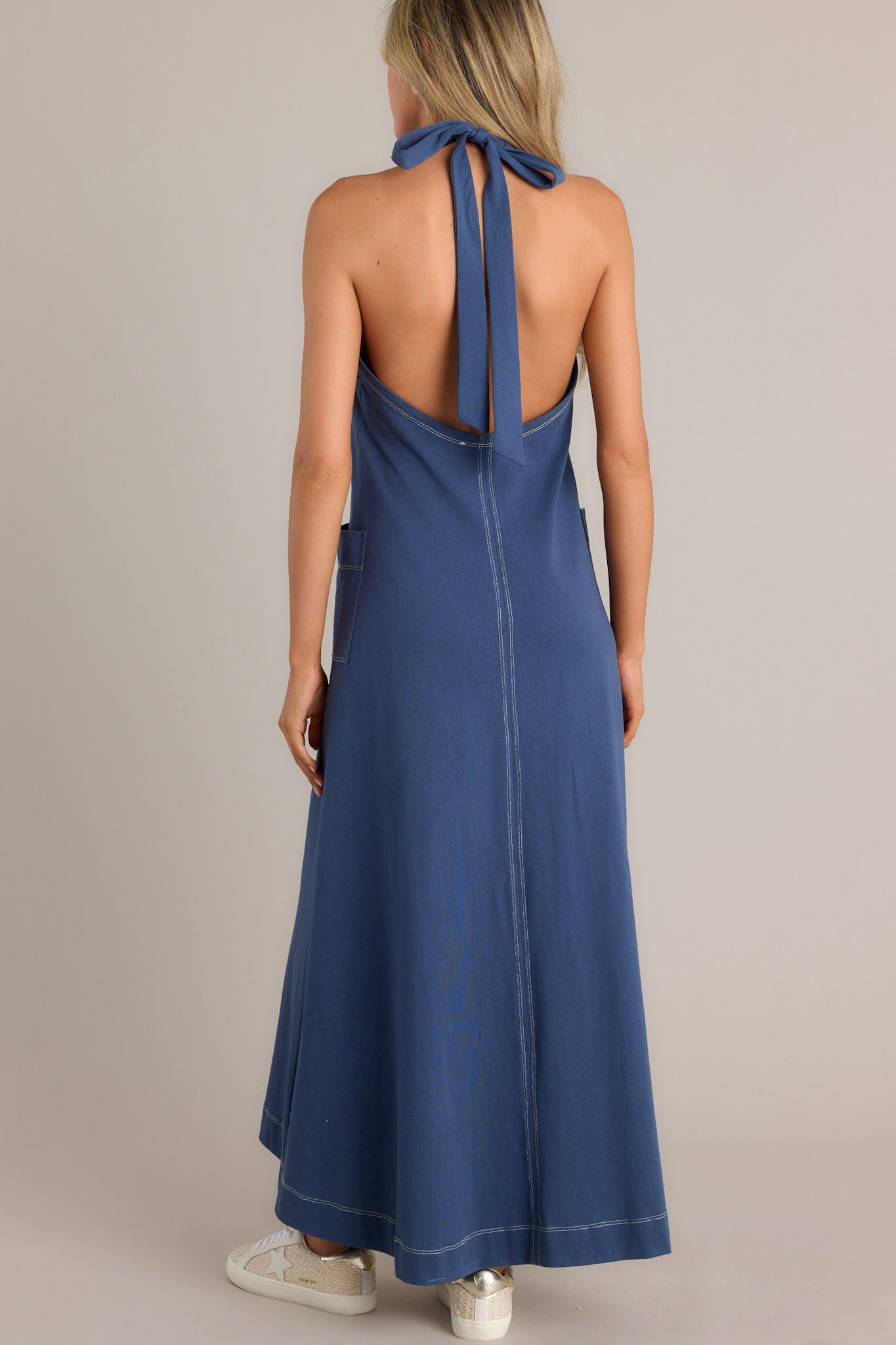 Back view of this Long blue dress with a halter neckline, deep V-front, and practical patch pockets.