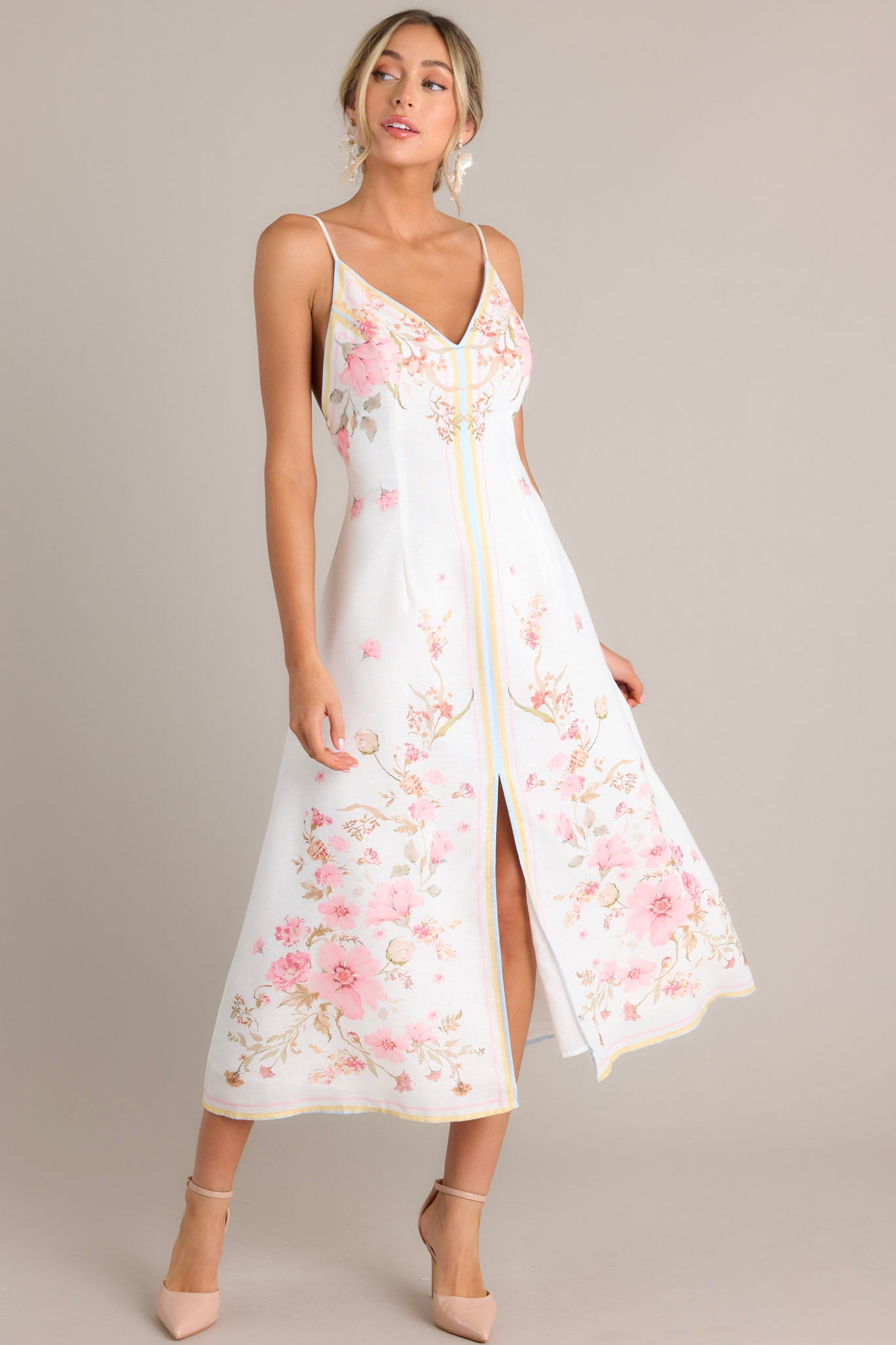 Angled full body view of this floral midi dress that features a v-neckline, thin adjustable self-tie straps, an open back, a discrete side zipper, a delicate floral pattern, and a front slit.