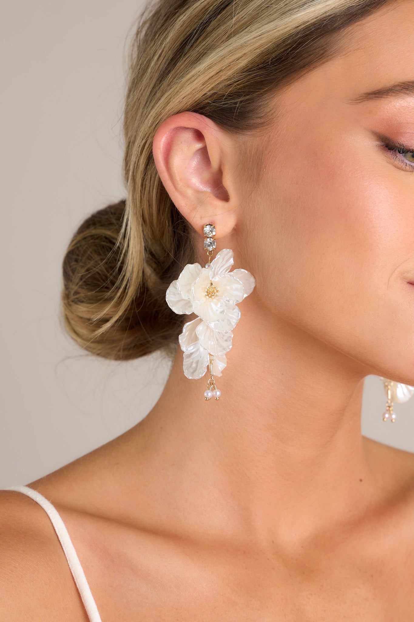 These flower drop earrings feature a diamond studs, gold hardware, pearlescent petals, and a pearl drop.