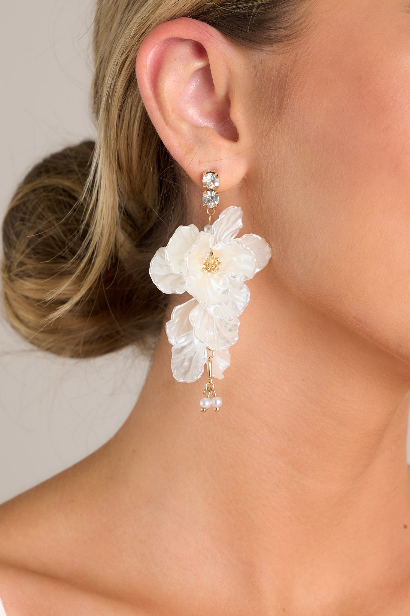 Close up view of these flower drop earrings that feature a diamond studs, gold hardware, pearlescent petals, and a pearl drop.