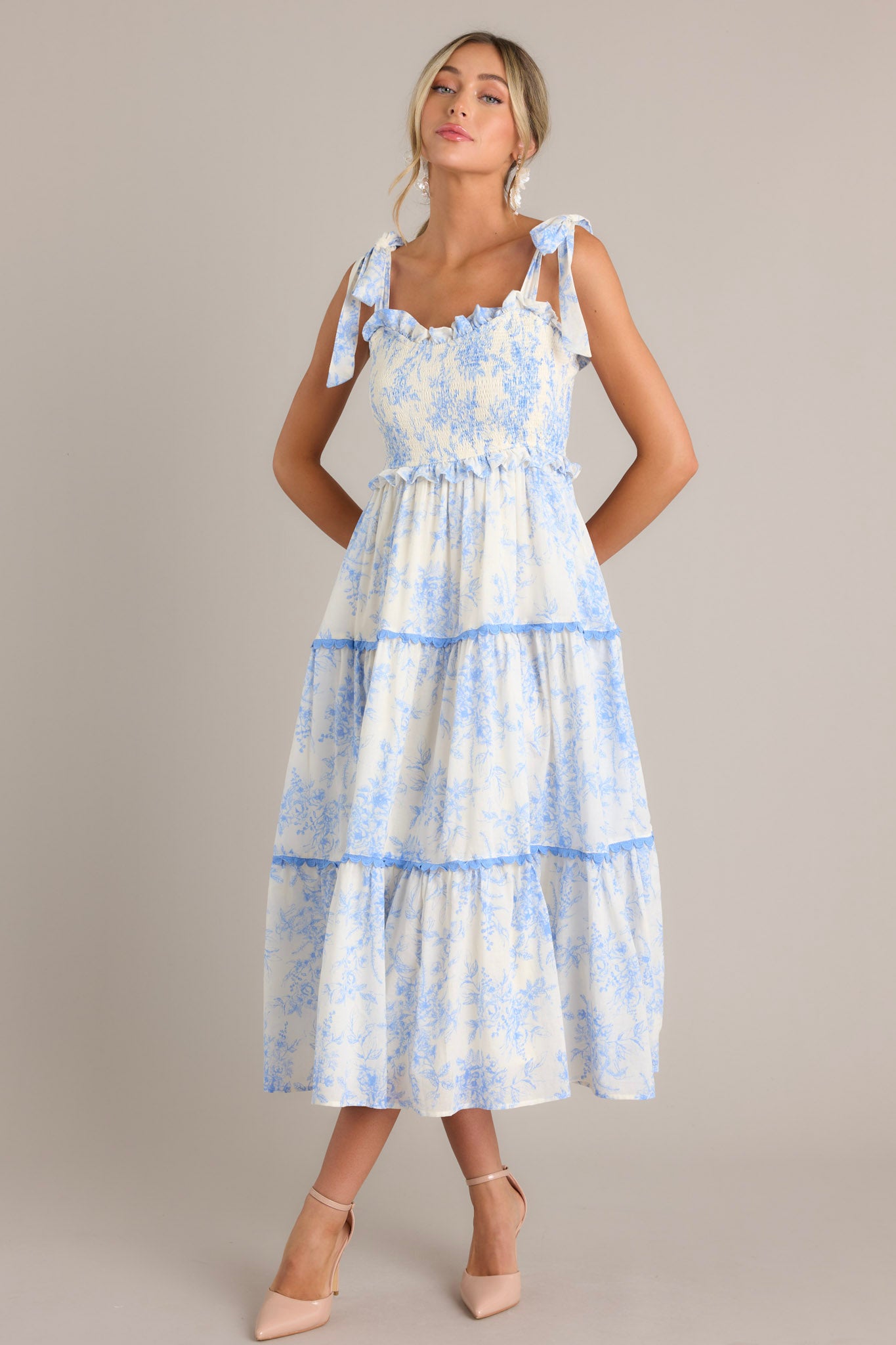 Full body view of this light blue midi dress that features a ruffled sweetheart neckline, self-tie straps, a fully smocked bodice, functional hip pockets, and scalloped tiers.