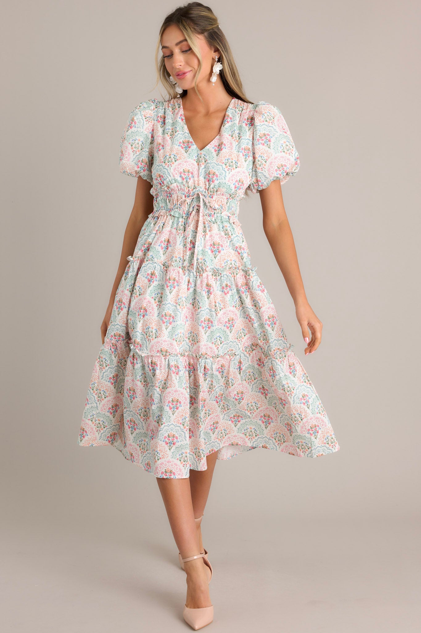 Angled front view of this floral midi dress that features a v-neckline, a smocked waistband, self-tie waist features, a tiered design, and short elastic cuffed puff sleeves.