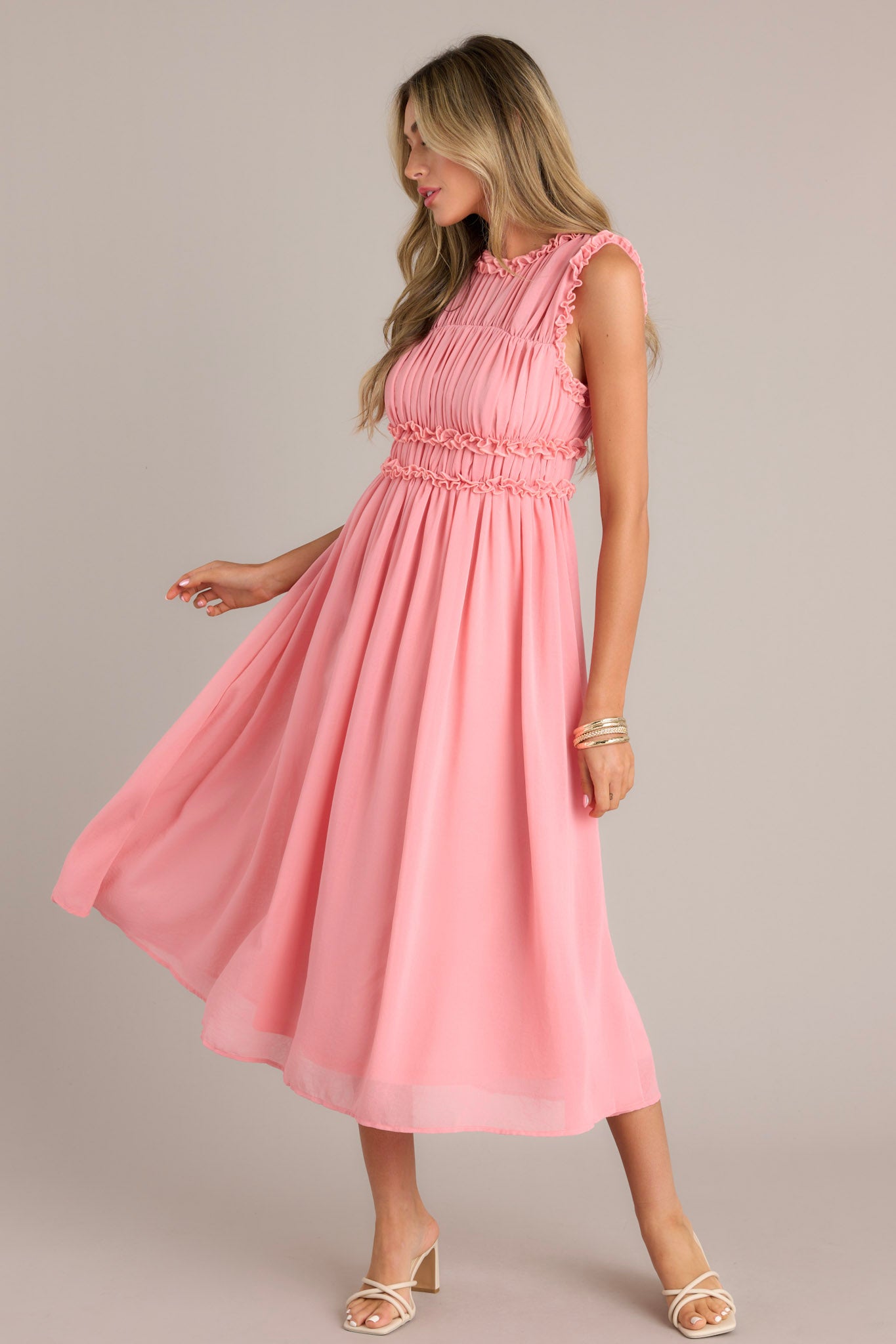 This dress in a pink coral hue features a high neckline with ruffles, a zipper closure at the back, and a keyhole opening.