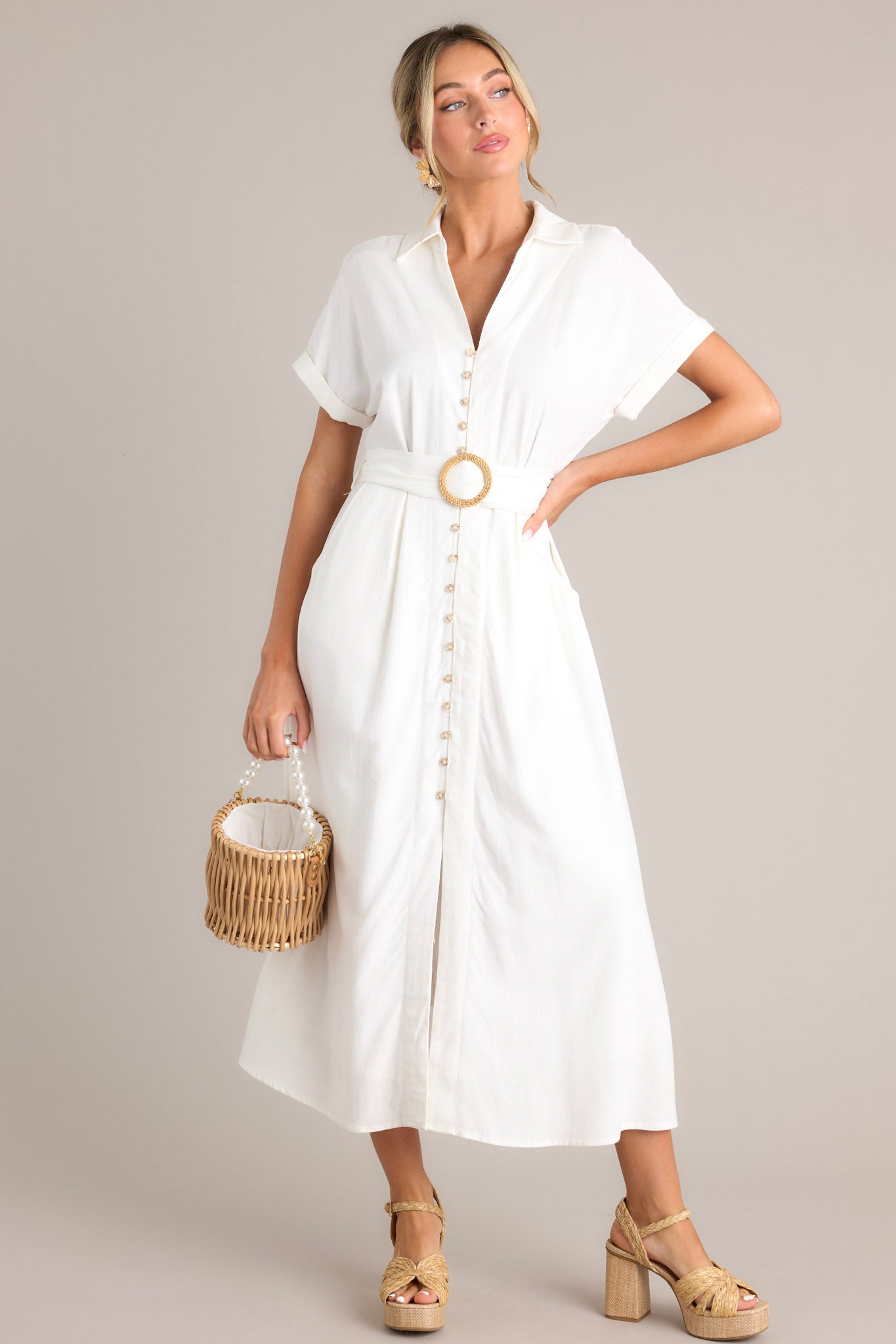 Full body view of this white maxi dress that features a collared v-neckline, a functional button front, a pull-through belt, functional hip pockets, a front slit, and cuffed short sleeves.