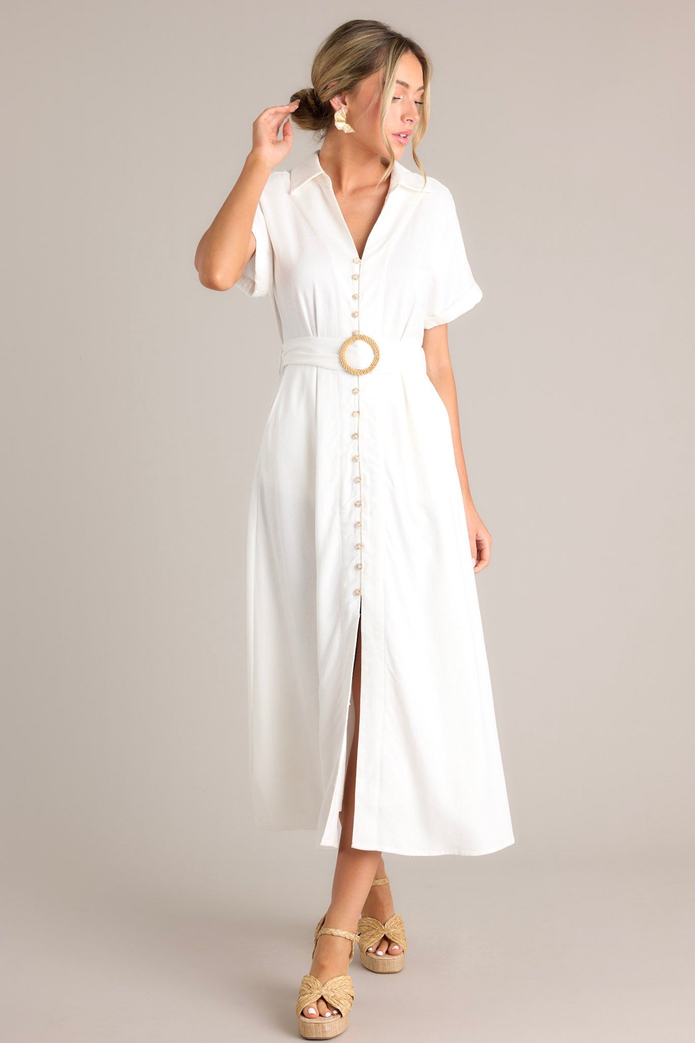 Front view of this white maxi dress that features a collared v-neckline, a functional button front, a pull-through belt, functional hip pockets, a front slit, and cuffed short sleeves.