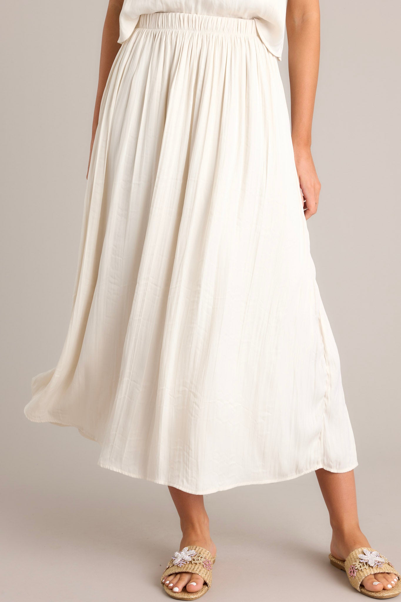 This midi sandstone skirt features a high waisted design, an elastic waistband, subtle pleats throughout, and a flowing silhouette.