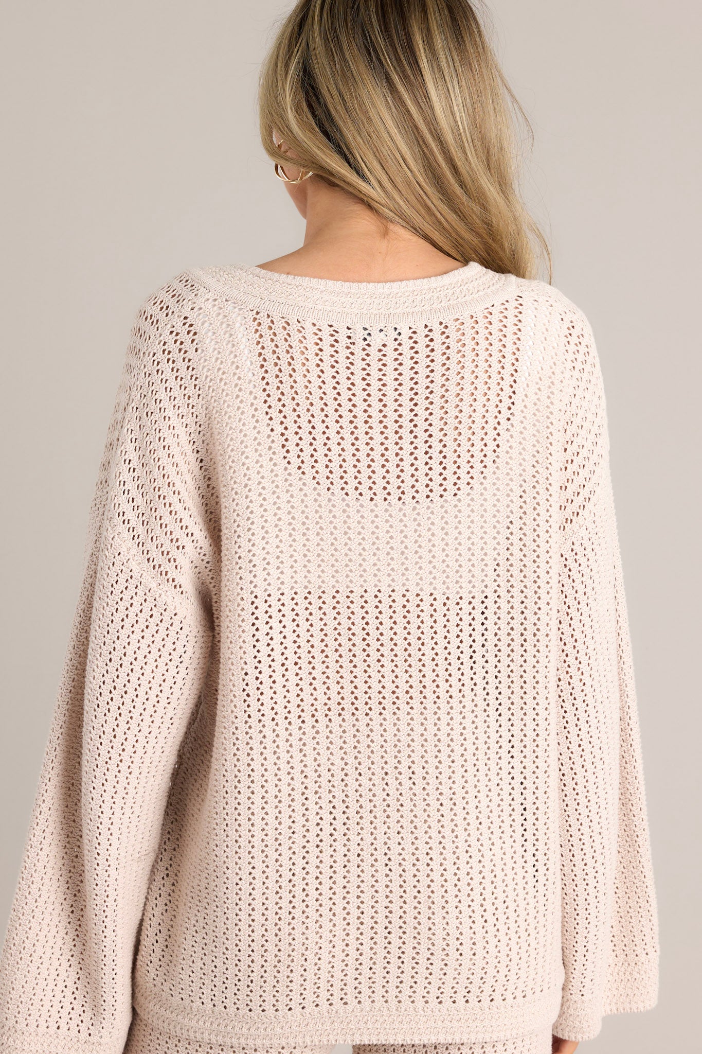 Back view of this natural sweater that features a v-neckline, an open knit design, a relaxed fit, and wide long sleeves.