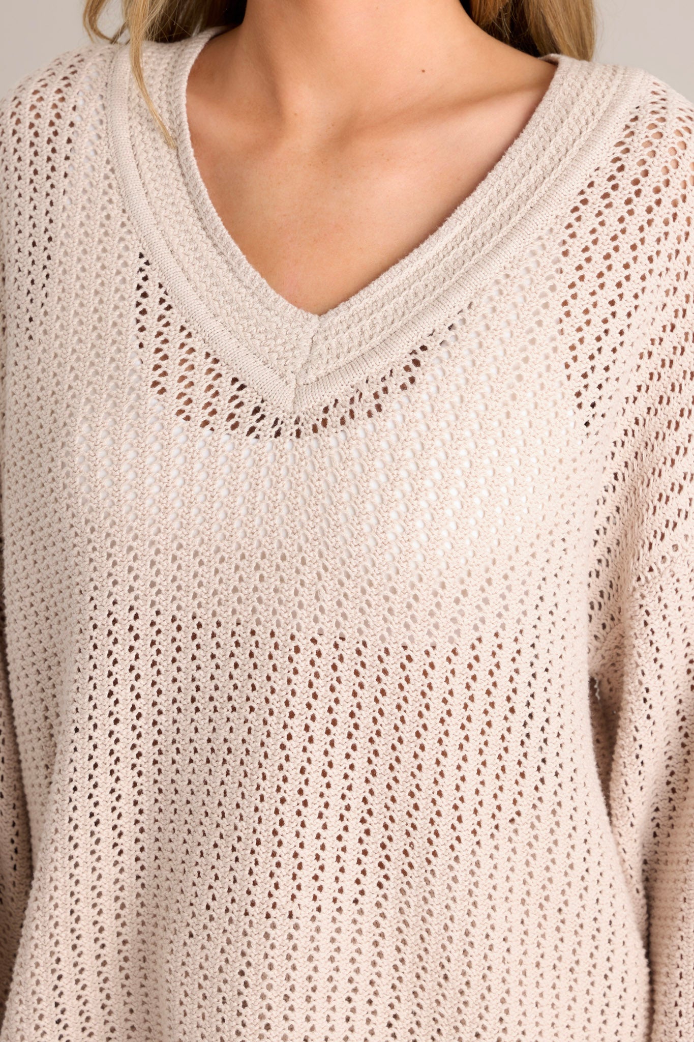 Close up view of this natural sweater that features a v-neckline, an open knit design, a relaxed fit, and wide long sleeves.