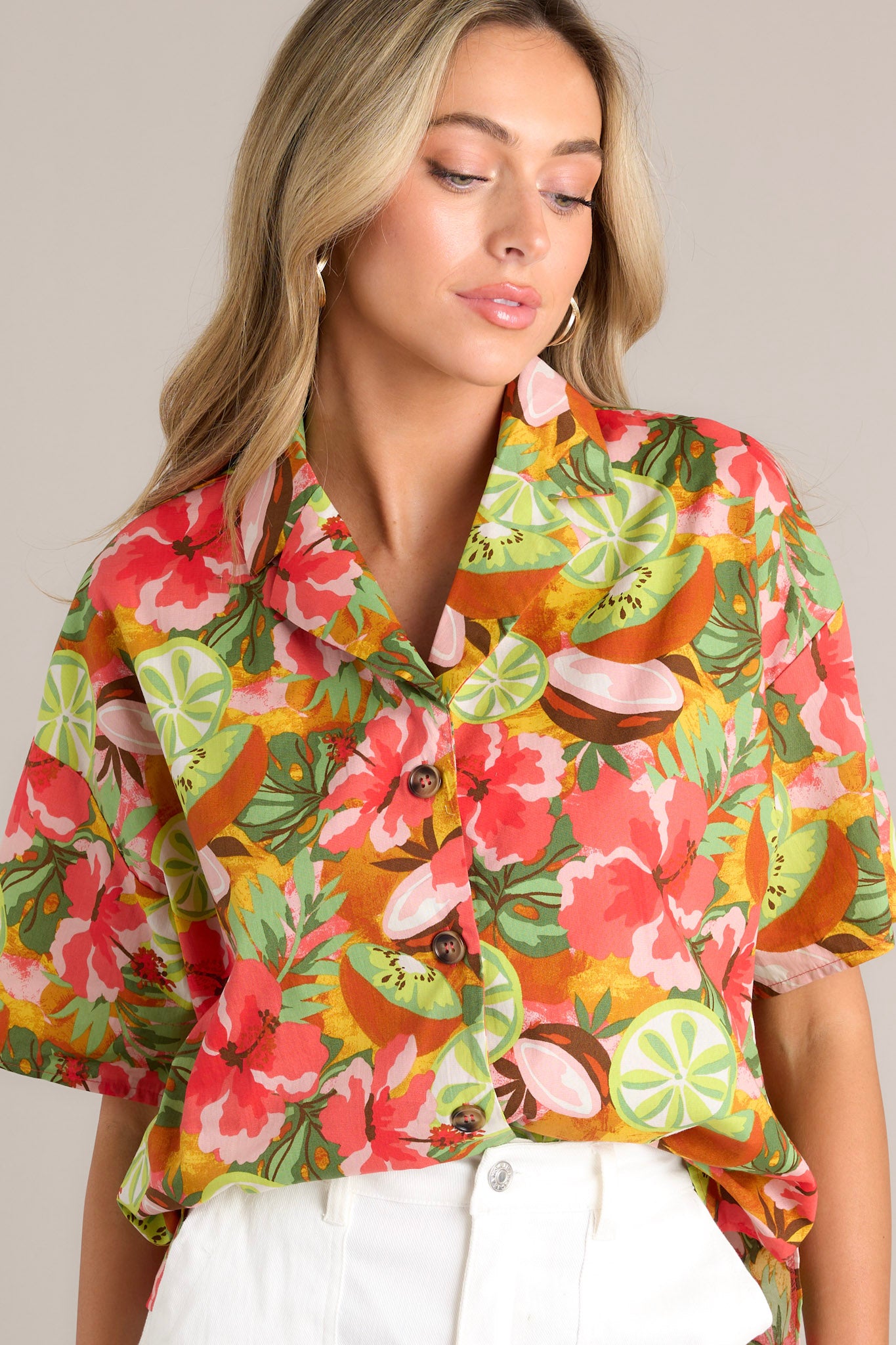 Angled close up front view of this coral tropical print top that features a collared neckline, fully functional buttons down the front, a citrus floral print design, and a slightly cropped fit.