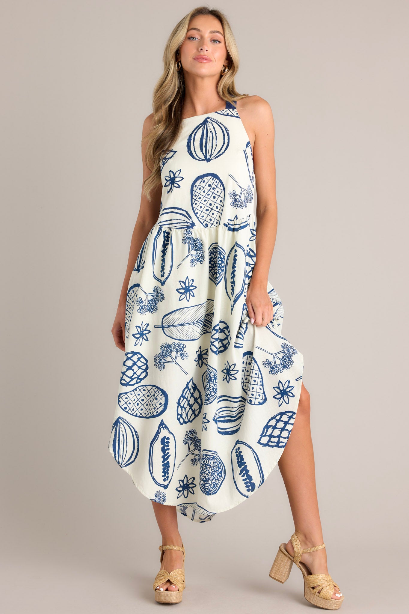 Full body view of this navy midi dress that features a square neckline, self-tie straps that cross in the back, an open back, an elastic insert in the back of the waist, functional hip pockets, a unique print, and a scoop hemline.