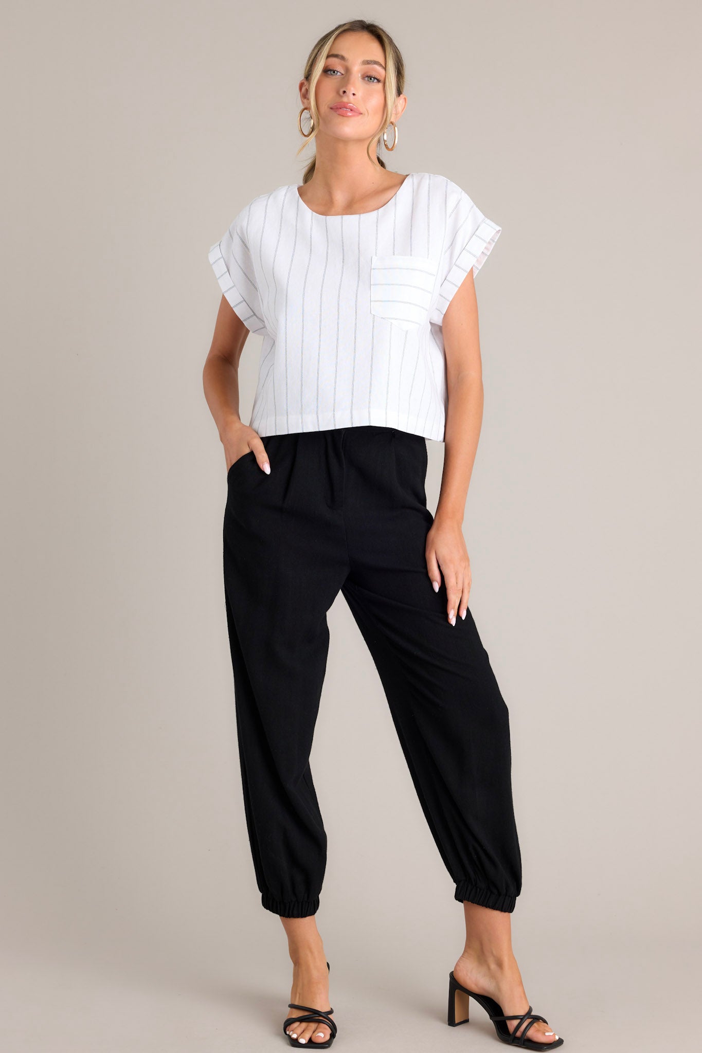 This white top features a crew neckline, functional buttons down the back, a functional breast pocket, cuffed wide short sleeves, and a cropped hemline.