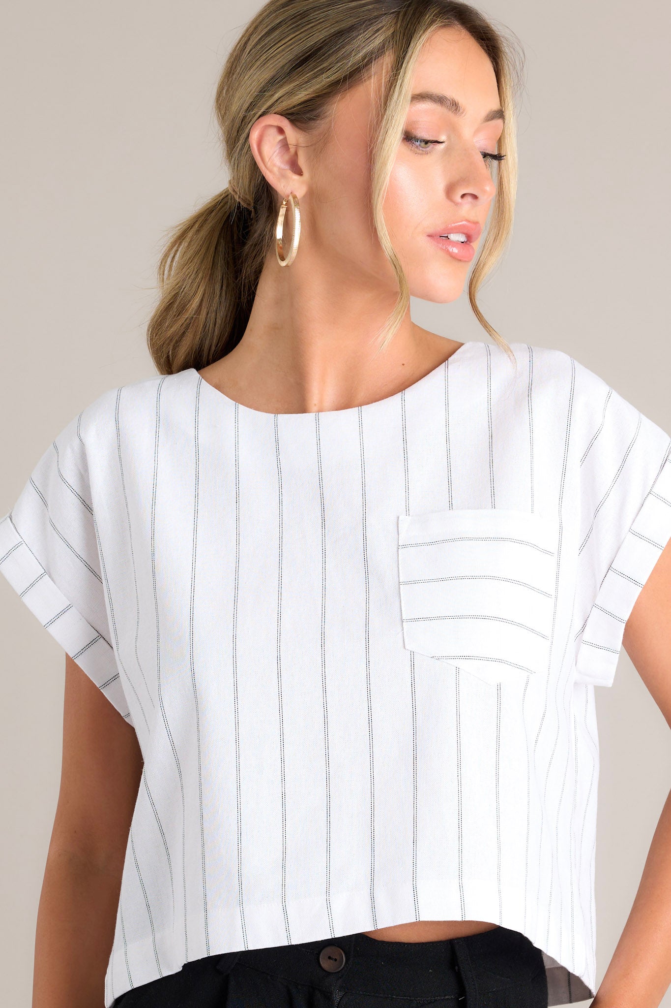 Front view of this white top that features a crew neckline, functional buttons down the back, a functional breast pocket, cuffed wide short sleeves, and a cropped hemline.