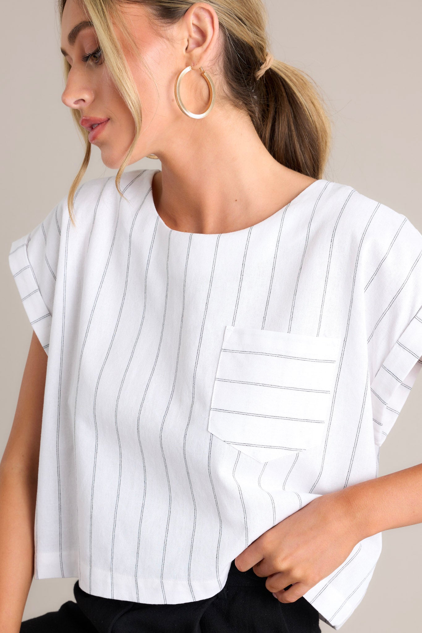 This white top features a crew neckline, functional buttons down the back, a functional breast pocket, cuffed wide short sleeves, and a cropped hemline.