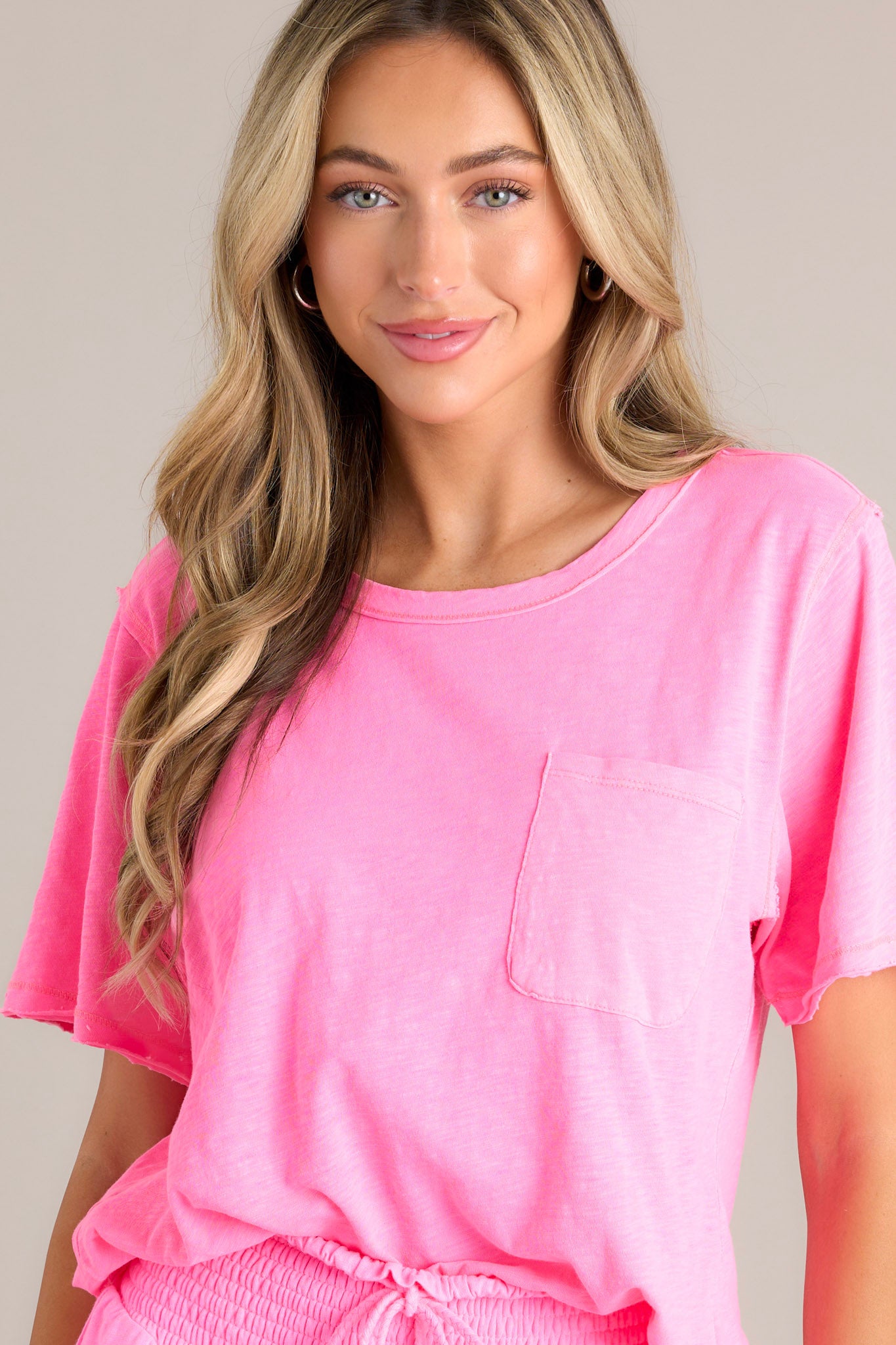 Front view of this neon pink tee that features a crew neckline, a functional breast pocket, a raw hemline, and short sleeves.