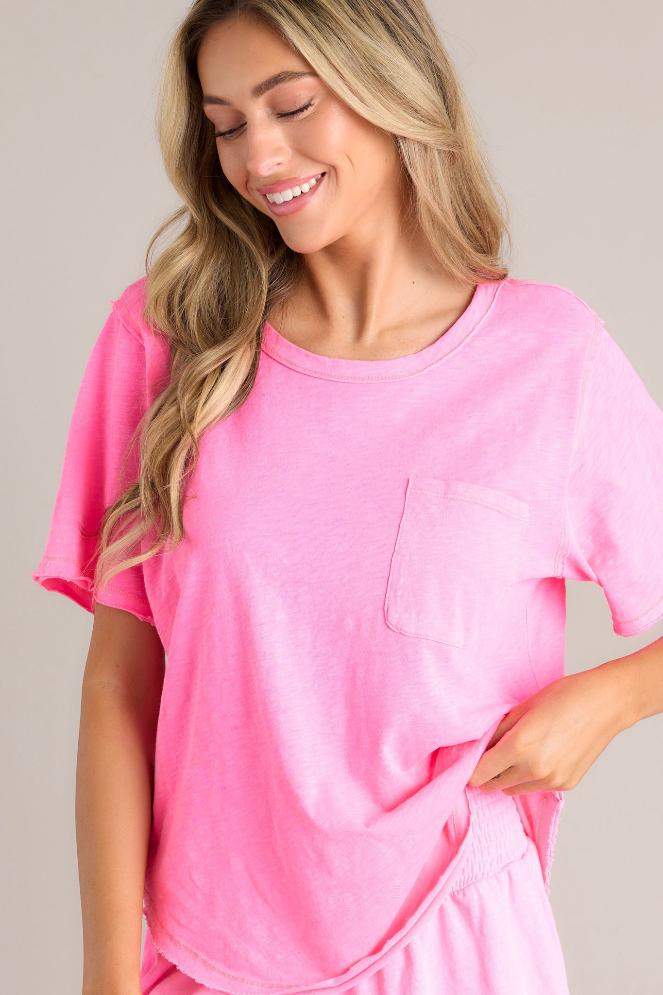 Angled front view of this neon pink tee that features a crew neckline, a functional breast pocket, a raw hemline, and short sleeves.