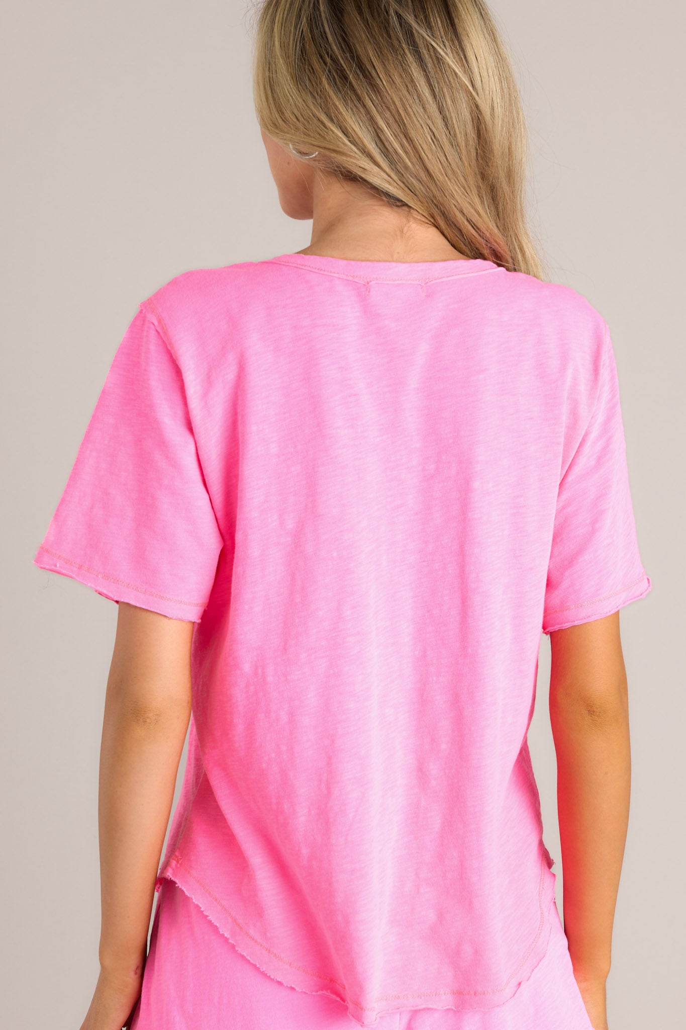 Back view of this neon pink tee that features a crew neckline, a functional breast pocket, a raw hemline, and short sleeves.