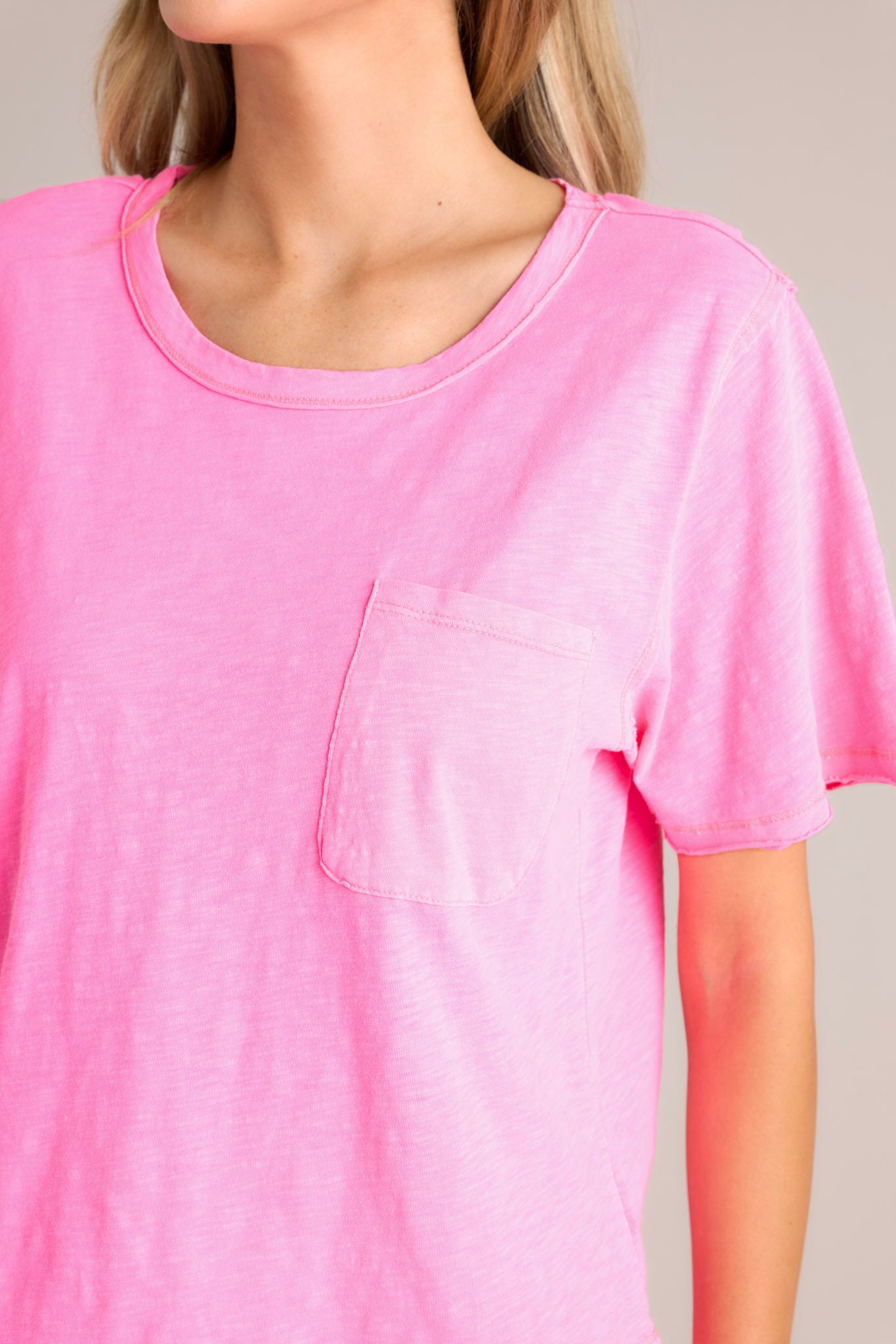 Close up view of this neon pink tee that features a crew neckline, a functional breast pocket, a raw hemline, and short sleeves.