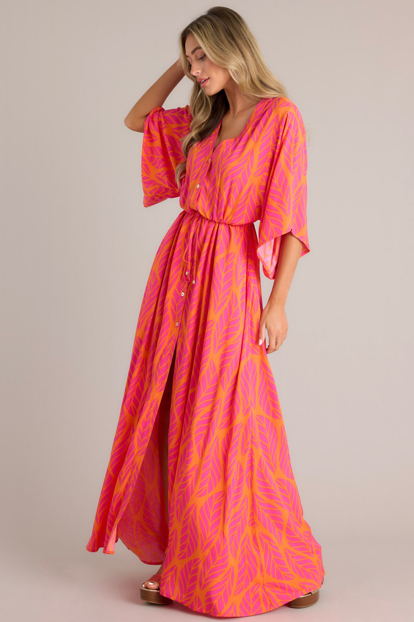 This hot pink maxi dress features a v-neckline, a functional button front, a self-tie drawstring waist, a flowing silhouette, and flowing half sleeves.