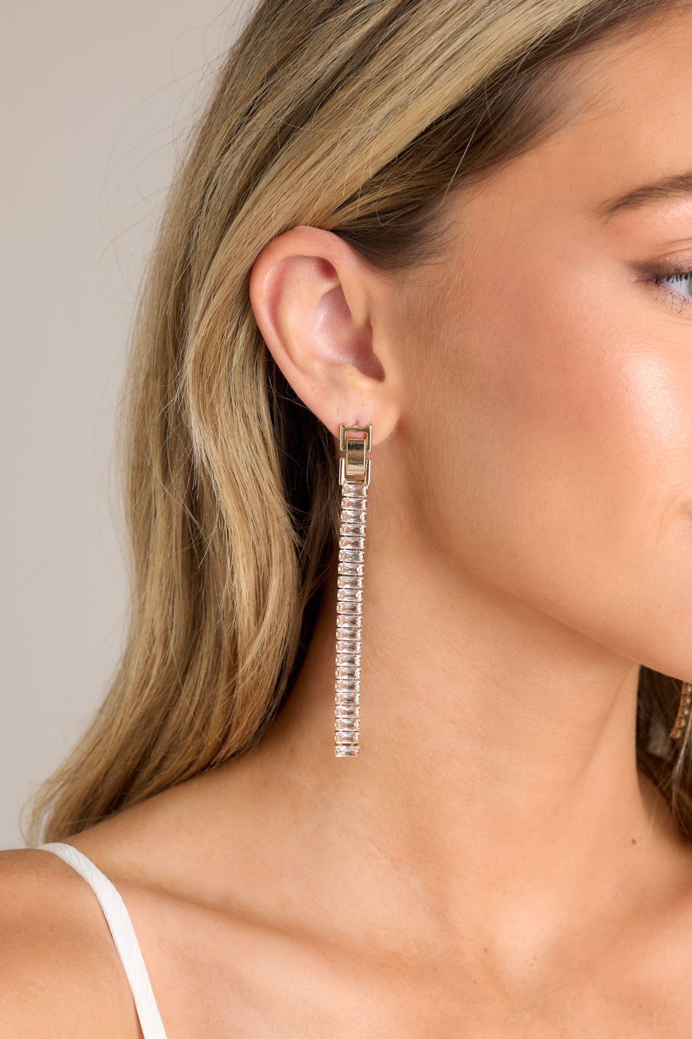 These earrings feature a stud in the style of a fold-over clasp, linked rectangular rhinestone dangles, and a secured post backing.