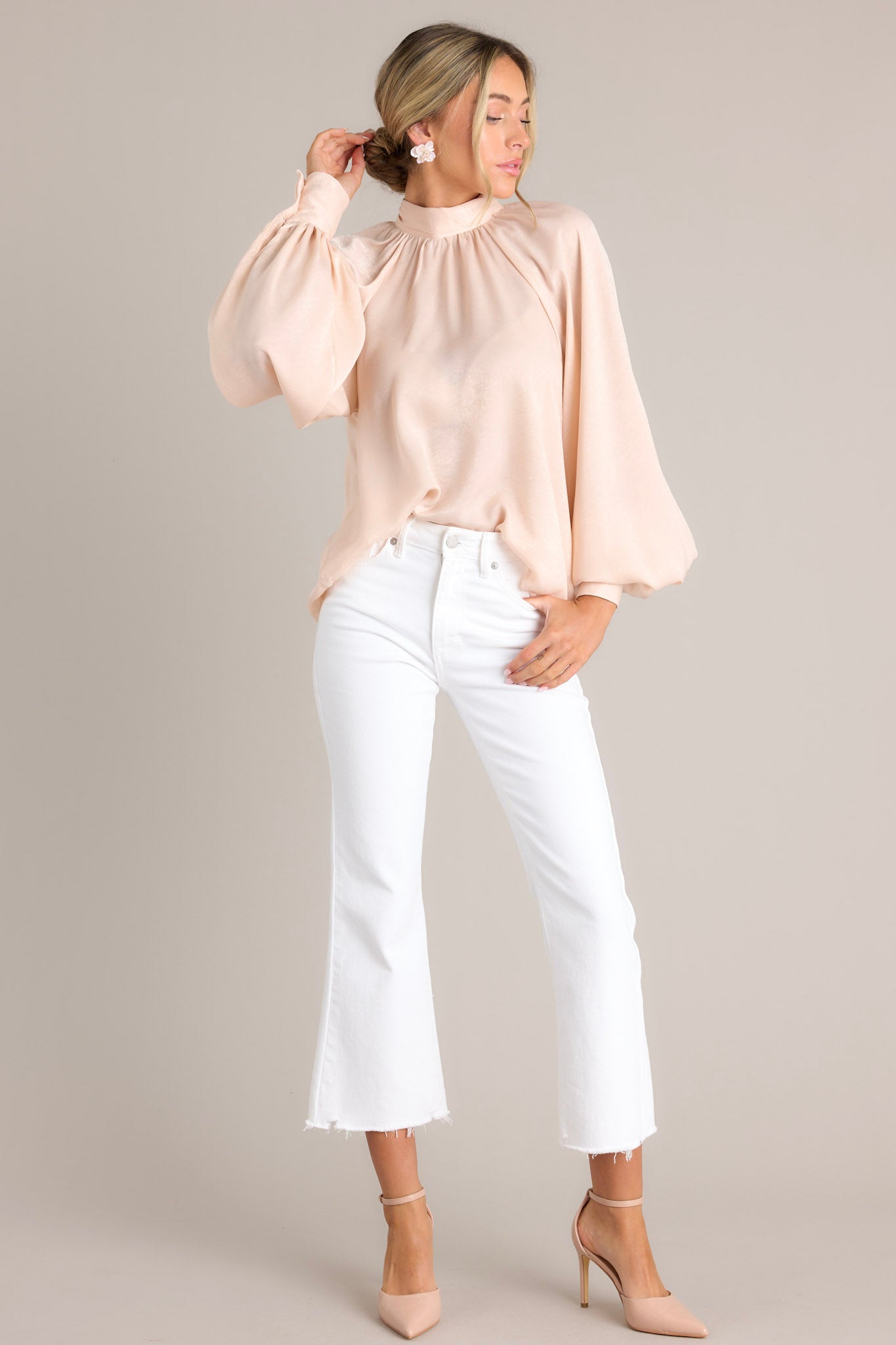 Front angled view of a top featuring a high neckline, balloon sleeves with buttons at the cuffs, an adjustable self-tie around the neck, and a flowy fit,