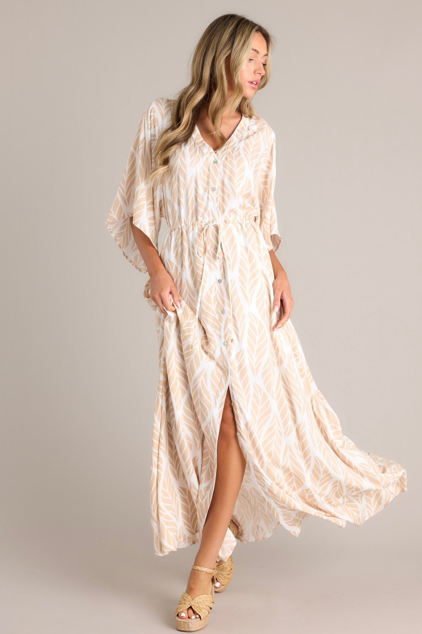 Front  view of this beige maxi dress that features a v-neckline, a functional button front, a self-tie drawstring waist, a flowing silhouette, and flowing half sleeves.