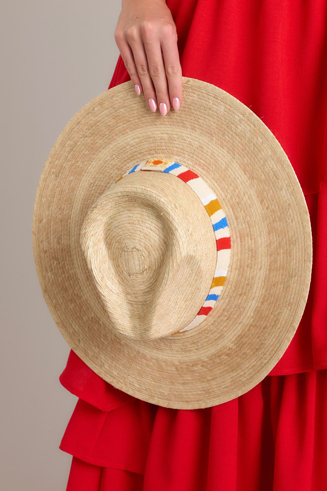 Close up view of This natural hat that is handmade with palm fronds and features a cotton band woven with primary color stripes.