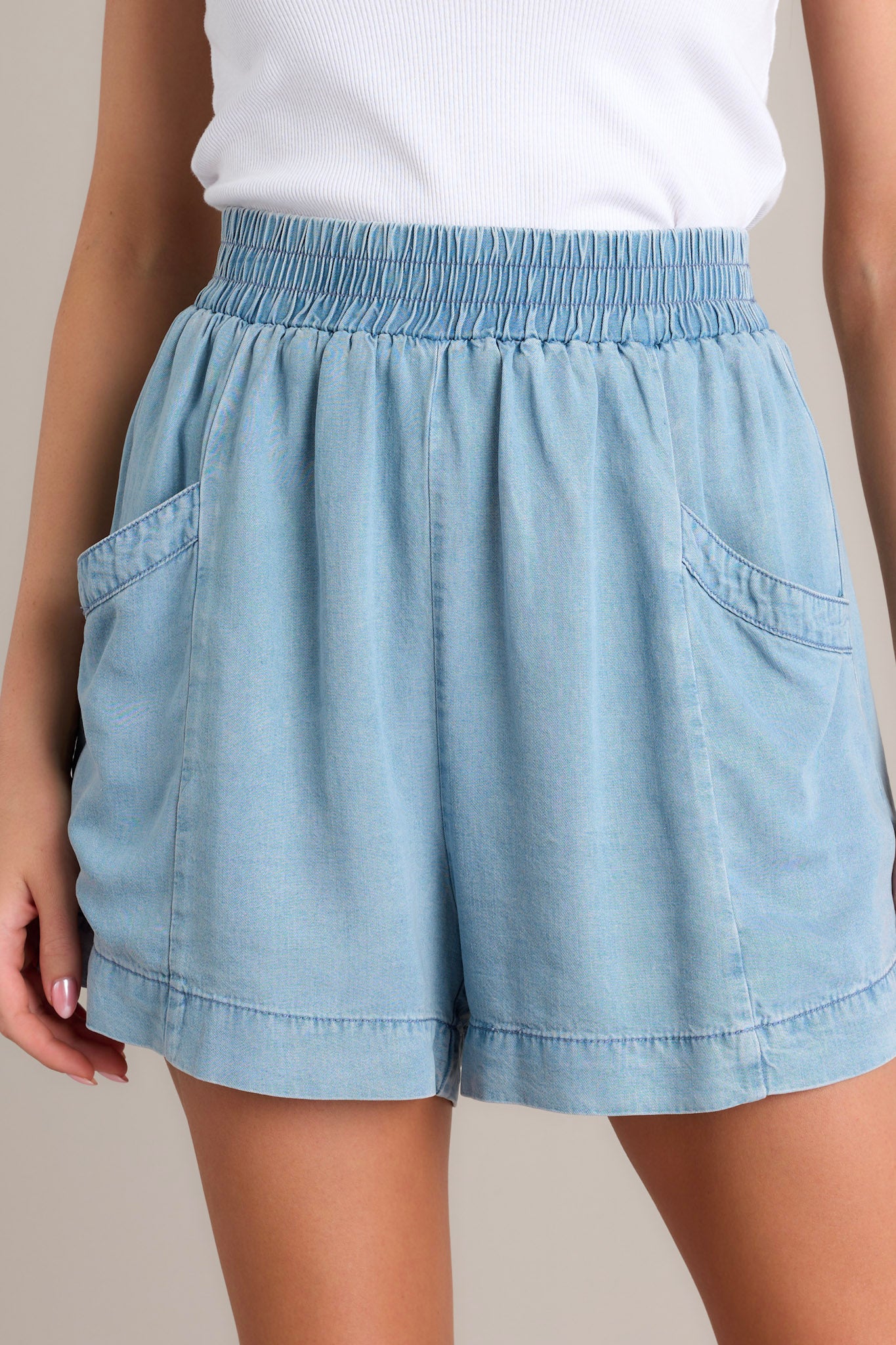 These light chambray shorts feature a high waisted design, an elastic waistband, large functional hip pockets, and a wide leg.
