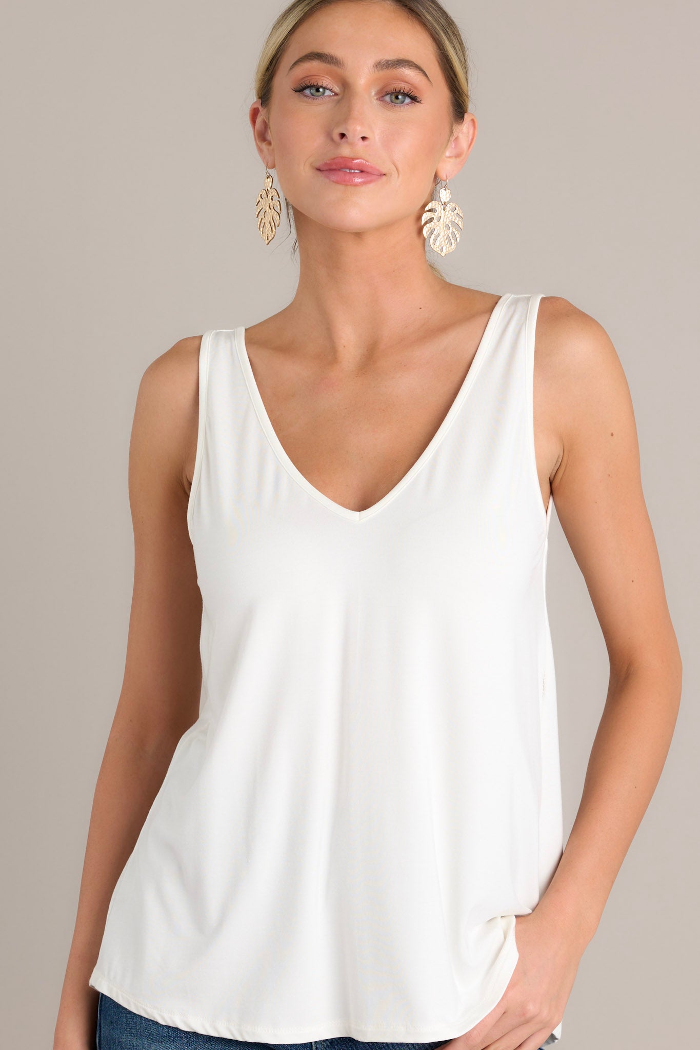 Front angled view of a white tank top featuring a v-neckline, a scoop bottom hem, and a buttery-soft feel