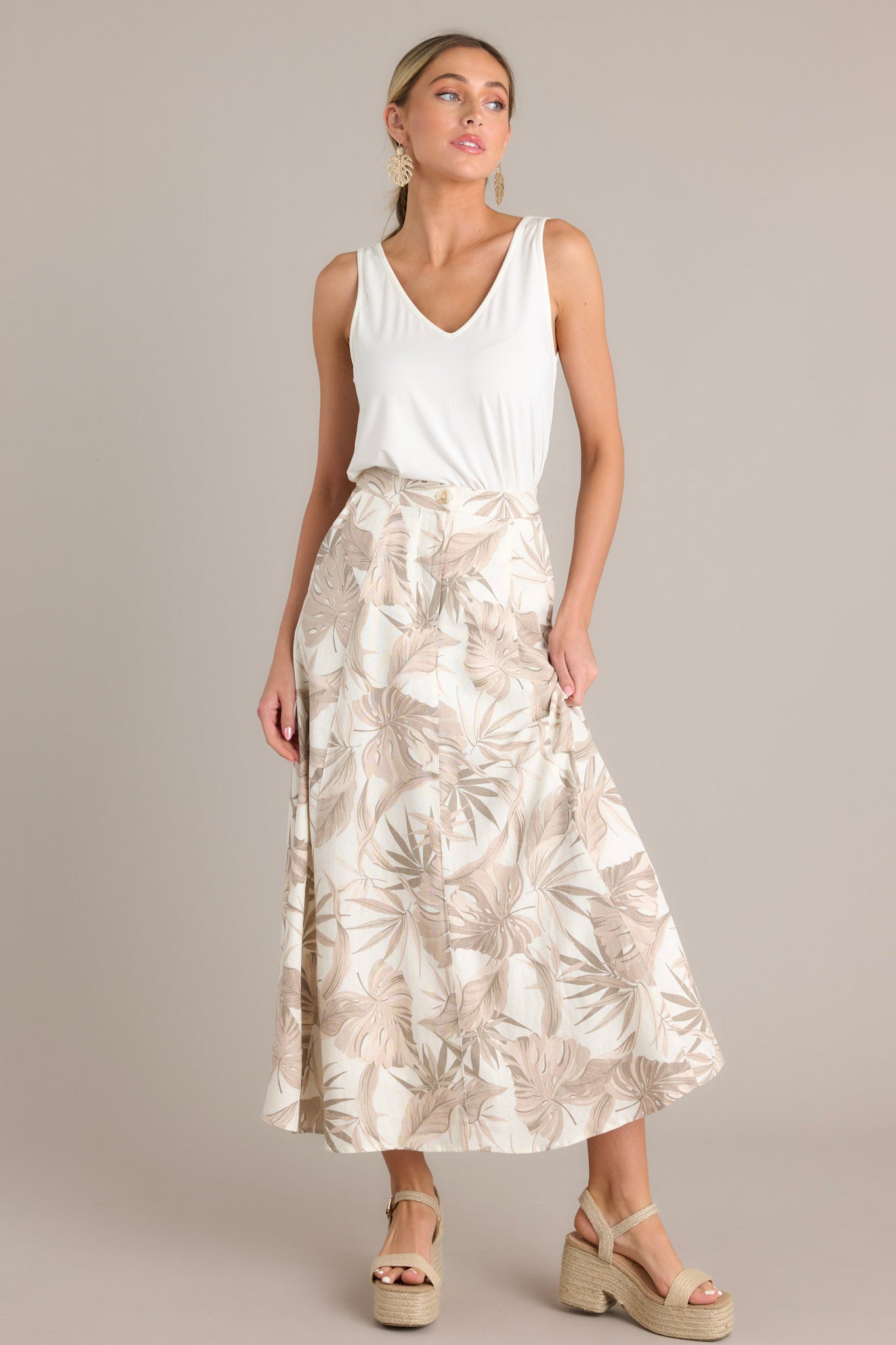 Full length view of a sandstone maxi skirt with a high waisted design, a button & zipper closure, functional hip pockets, and a flowing silhouette