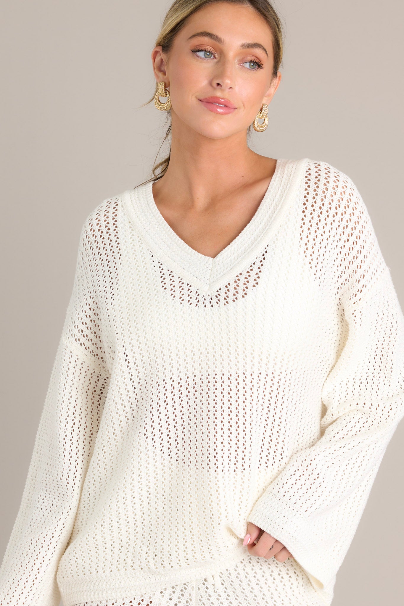 Front view of an ivory sweater featuring a v-neckline, a relaxed fit, an open knit design, and wide long sleeves.