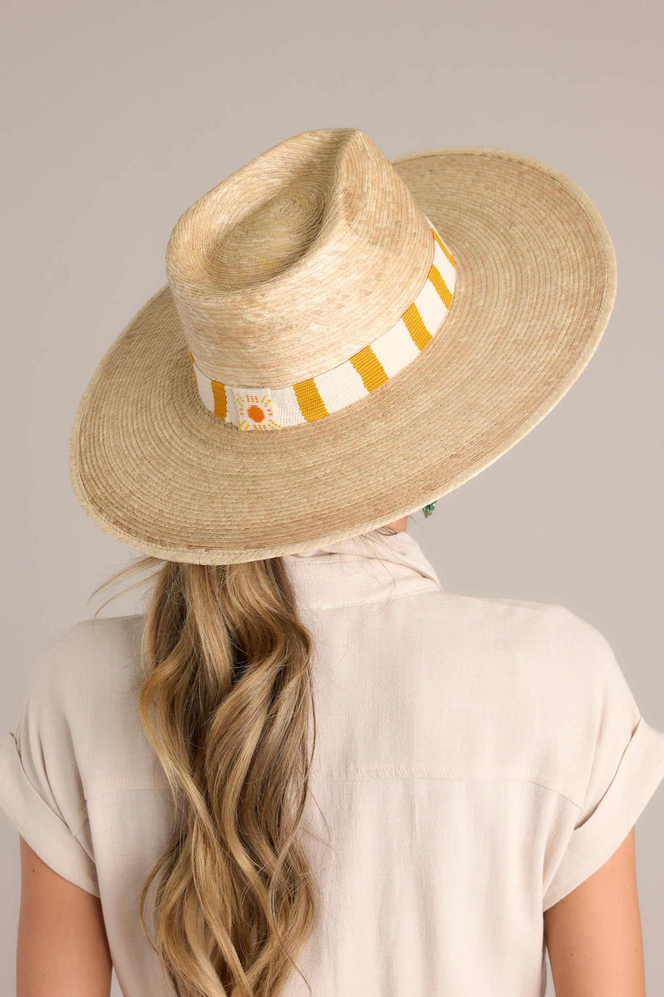 Back view of the Carmen Palm Hat that features a cotton woven band with mustard yellow and white stripes, and is handmade with palm fronds.