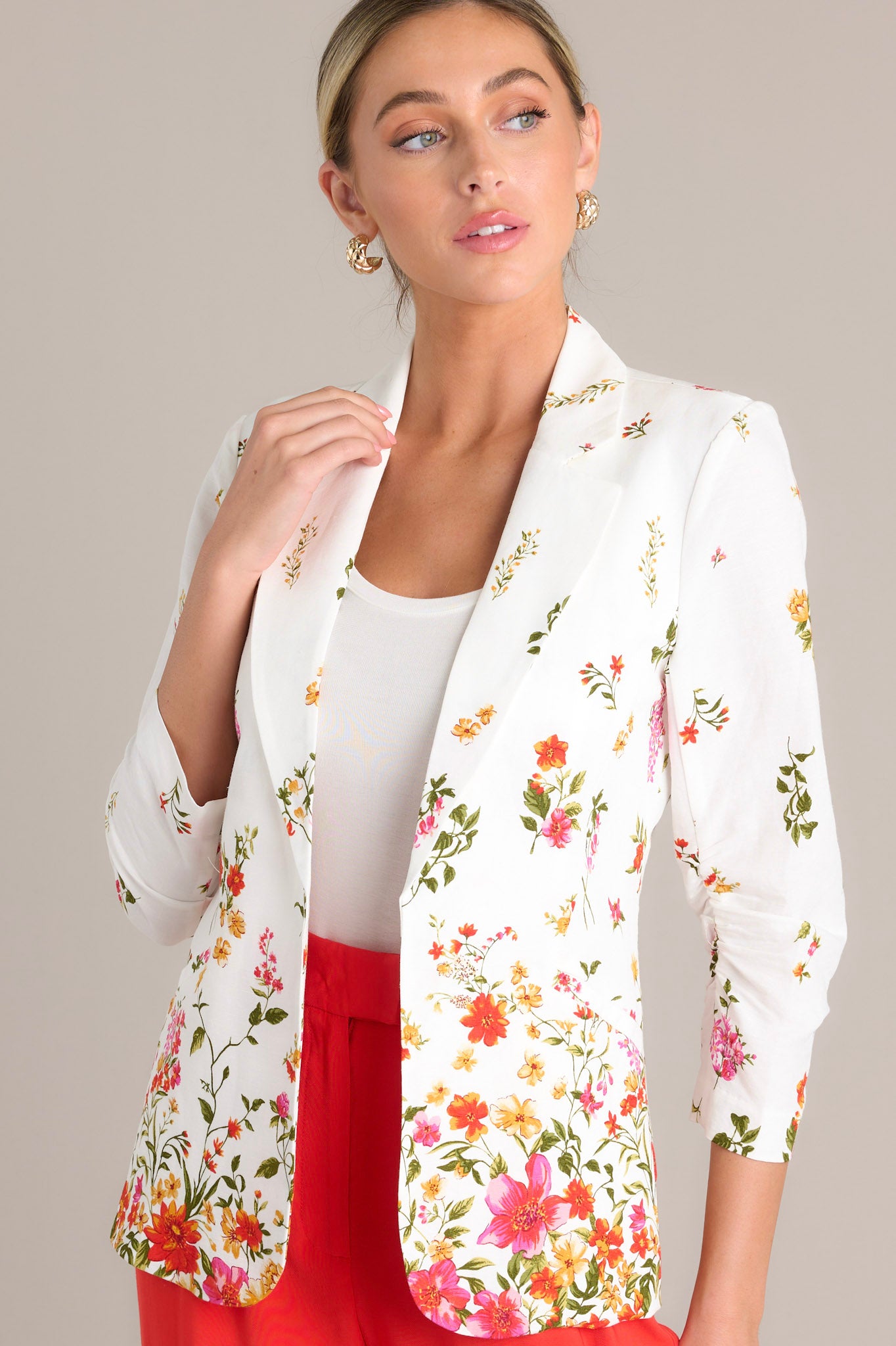 Front angled view of a blazer featuring a lapel collar, faux front pockets, 3/4 sleeves with a ruched detail, and a floral pattern throughout