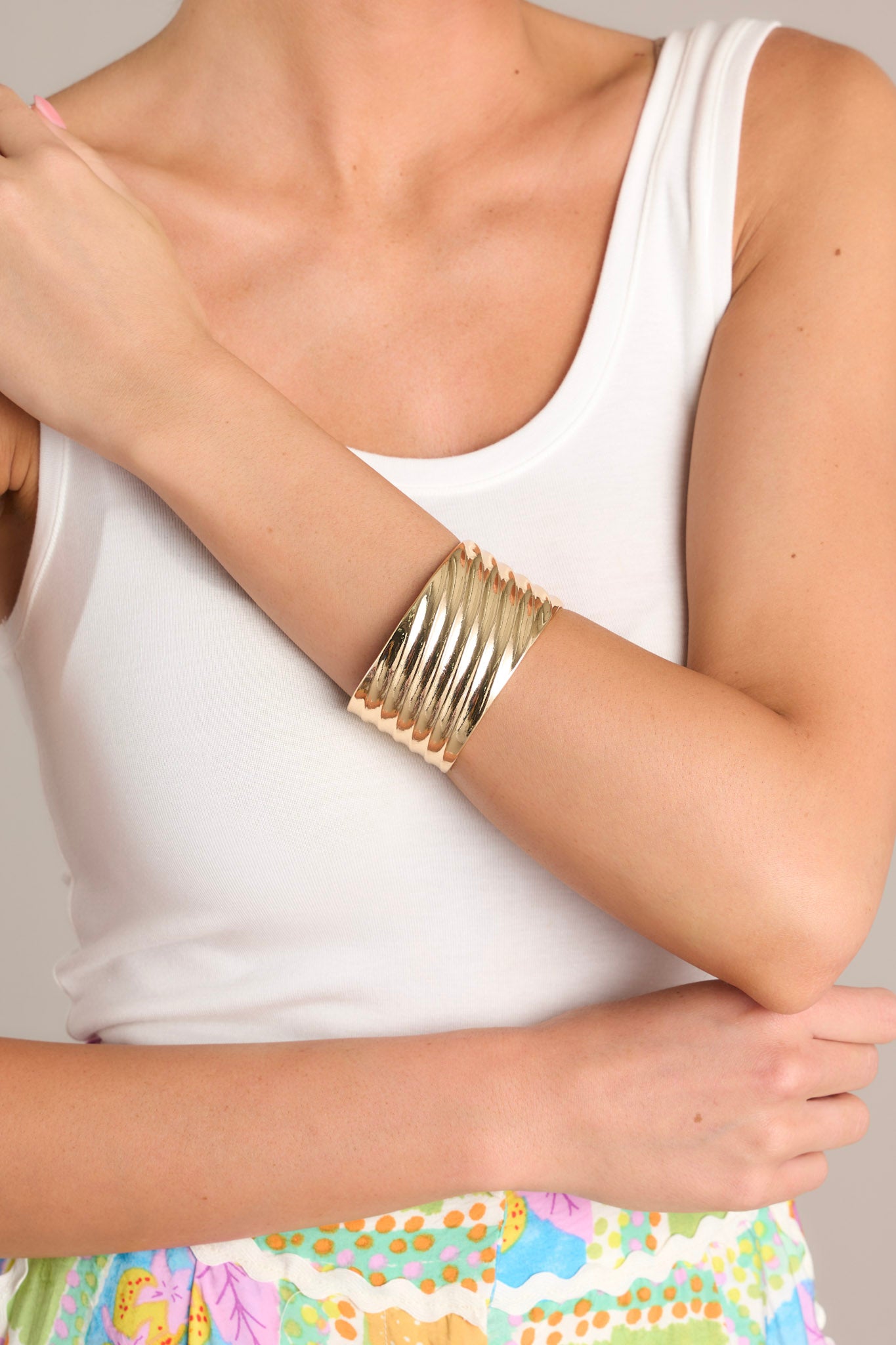 Close-up view of this gold cuff that features shiny hardware, a textured material, a thick band, and rounded edges.
