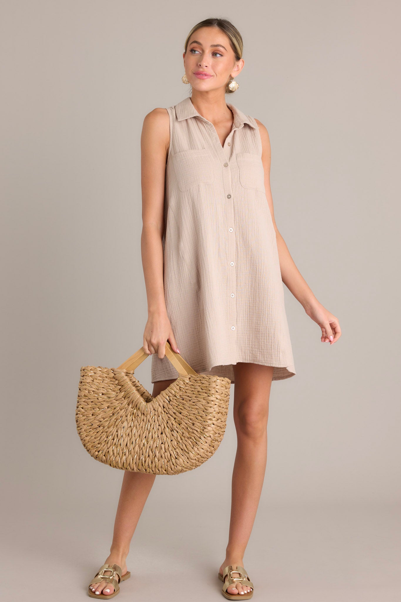 This taupe mini dress features a collared neckline, a functional button front, functional breast pockets, a lightweight material, and a sleeveless design.