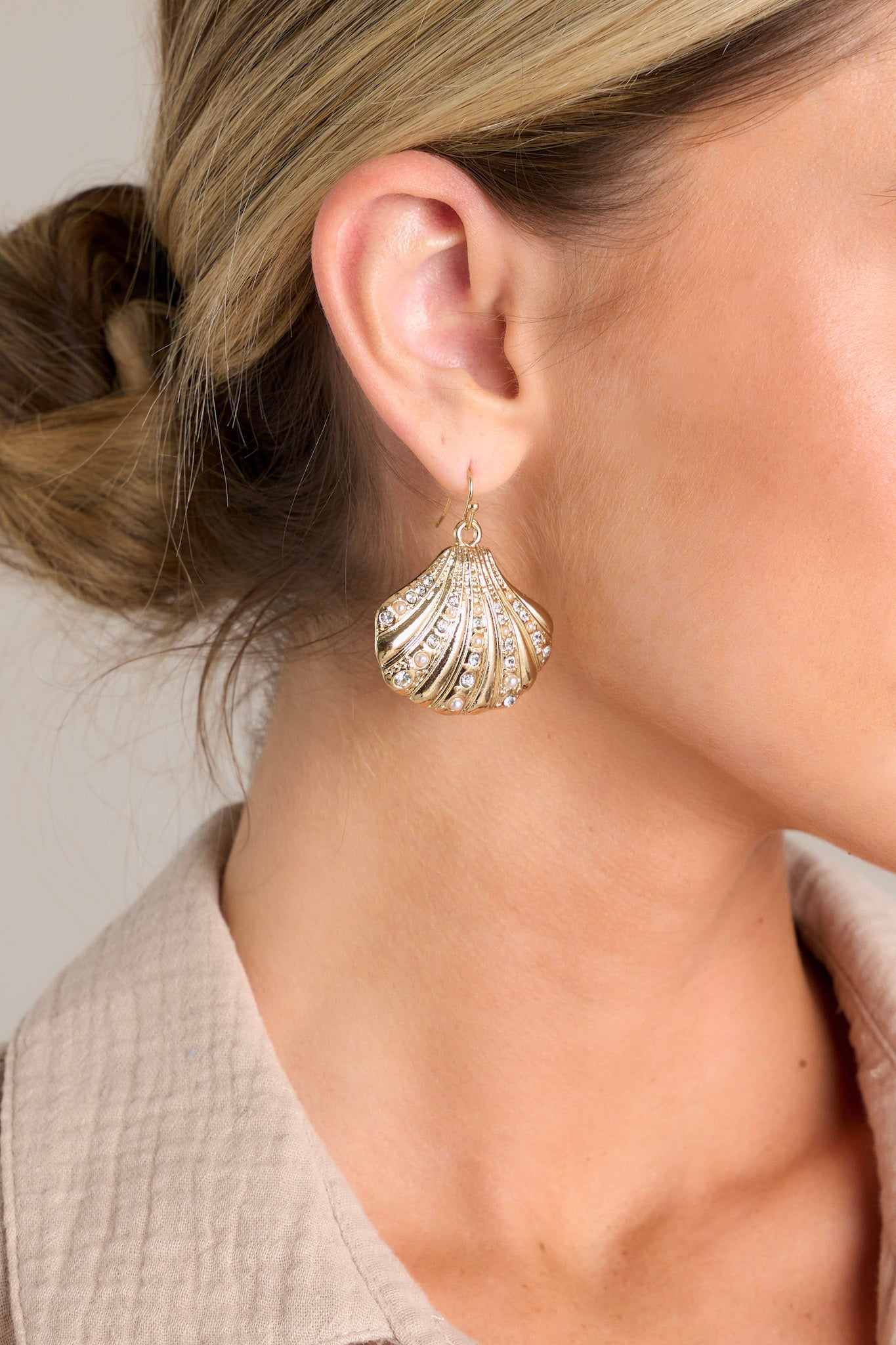 Close-up of these gold earrings that feature a gold seashell pendant adorned with rhinestones and faux pearls.