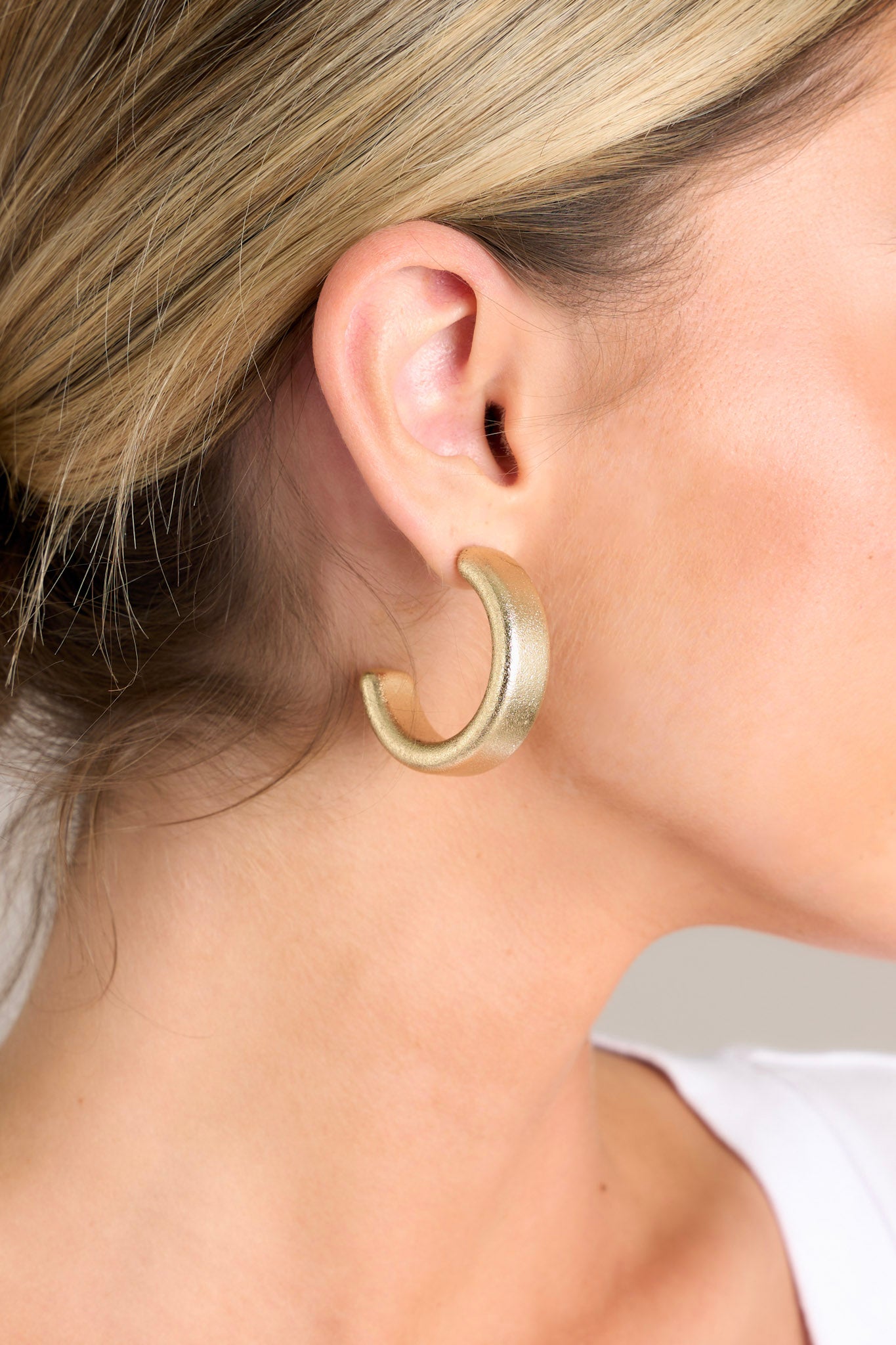 Close-up view of these gold hoop earrings that feature gold hardware, a thick incomplete hoop, and a textured finish.