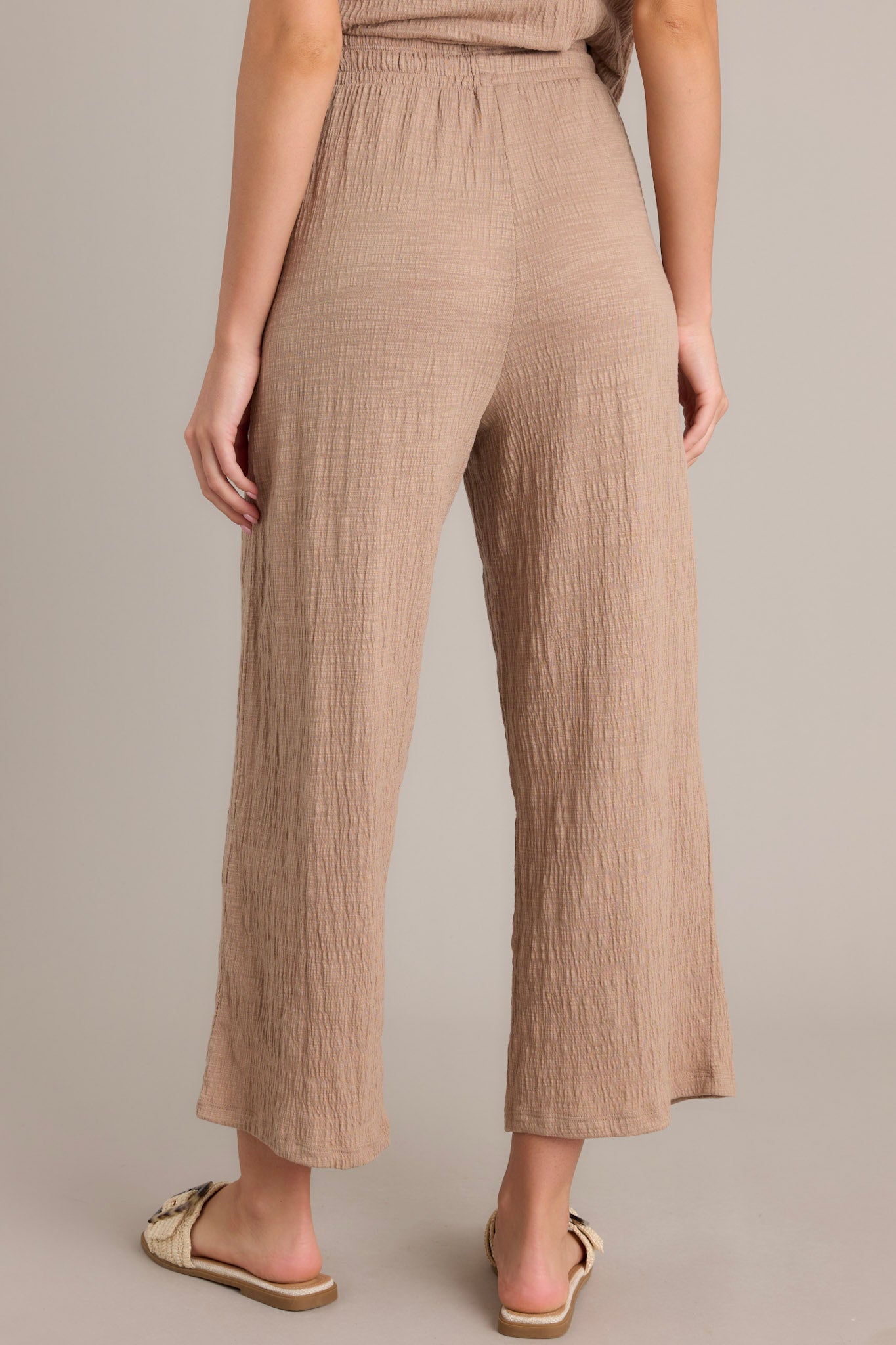 Back view of beige pants showcasing the high-waisted design, elastic waistband, textured material, and wide leg cut.