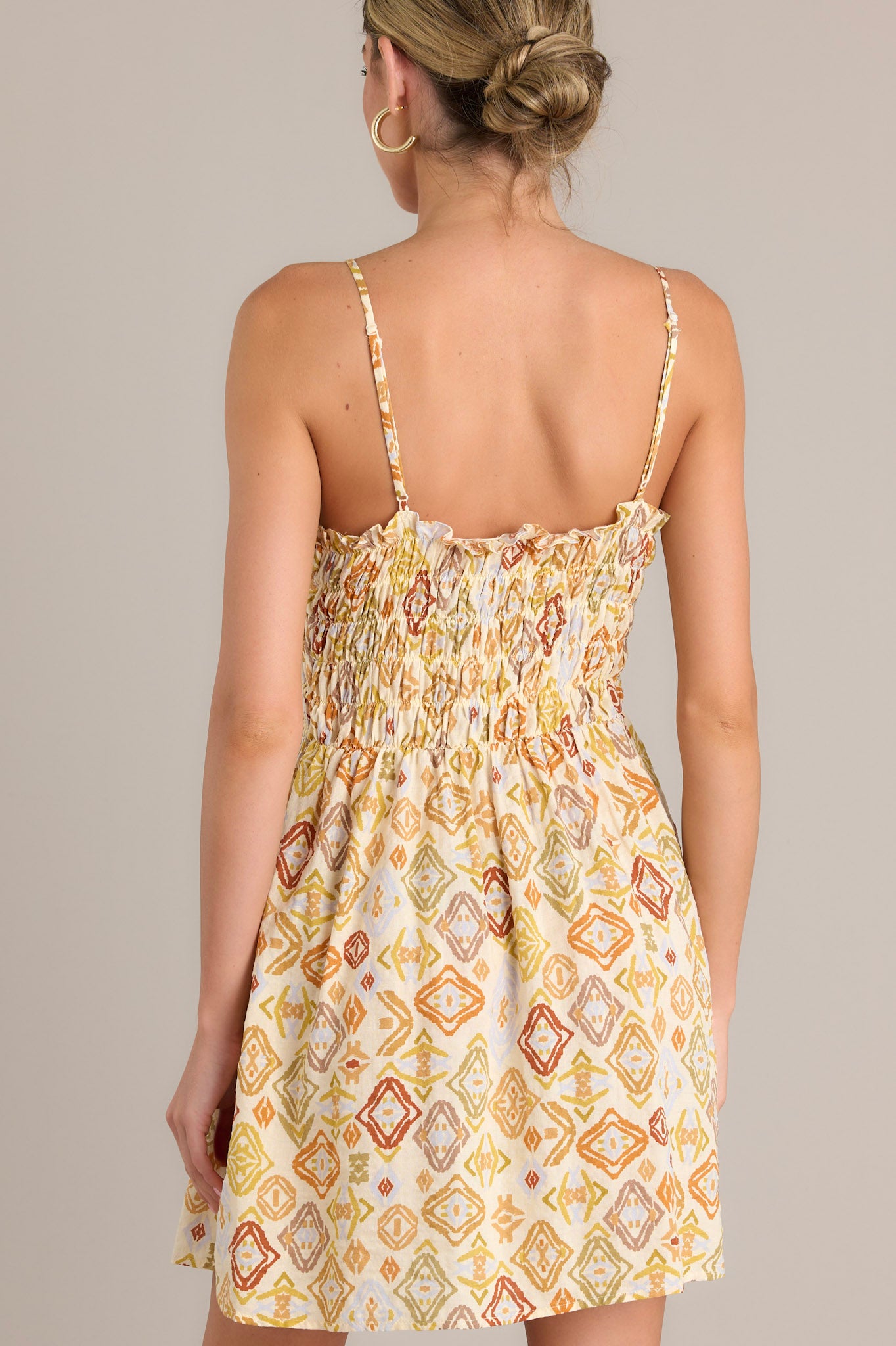 Back view of a beige mini dress showcasing the adjustable straps, smocked pleated bodice, and flowing skirt.