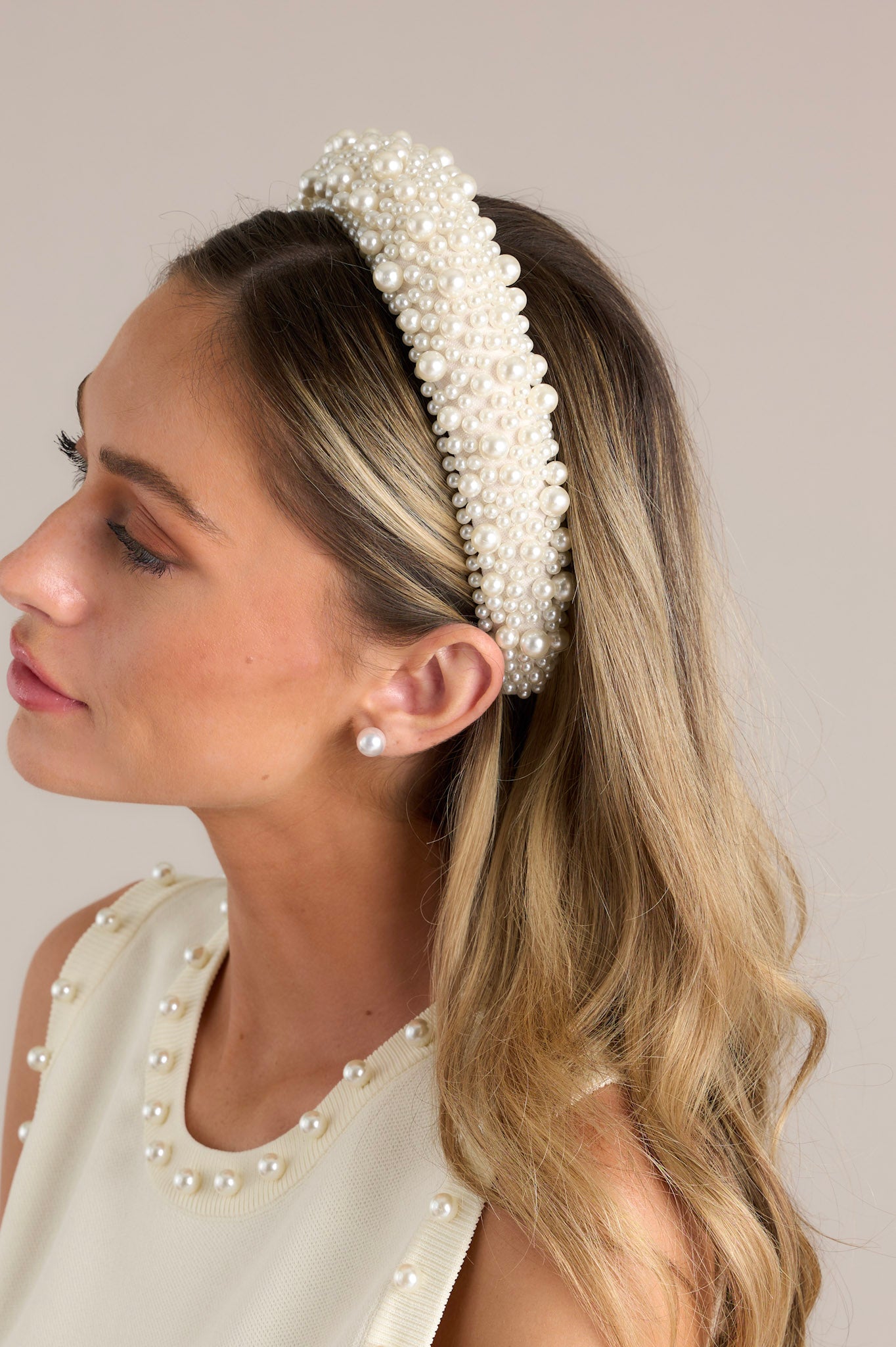 Side view of this headband that is adorned with many white faux pearls varying in size, and a thick band.