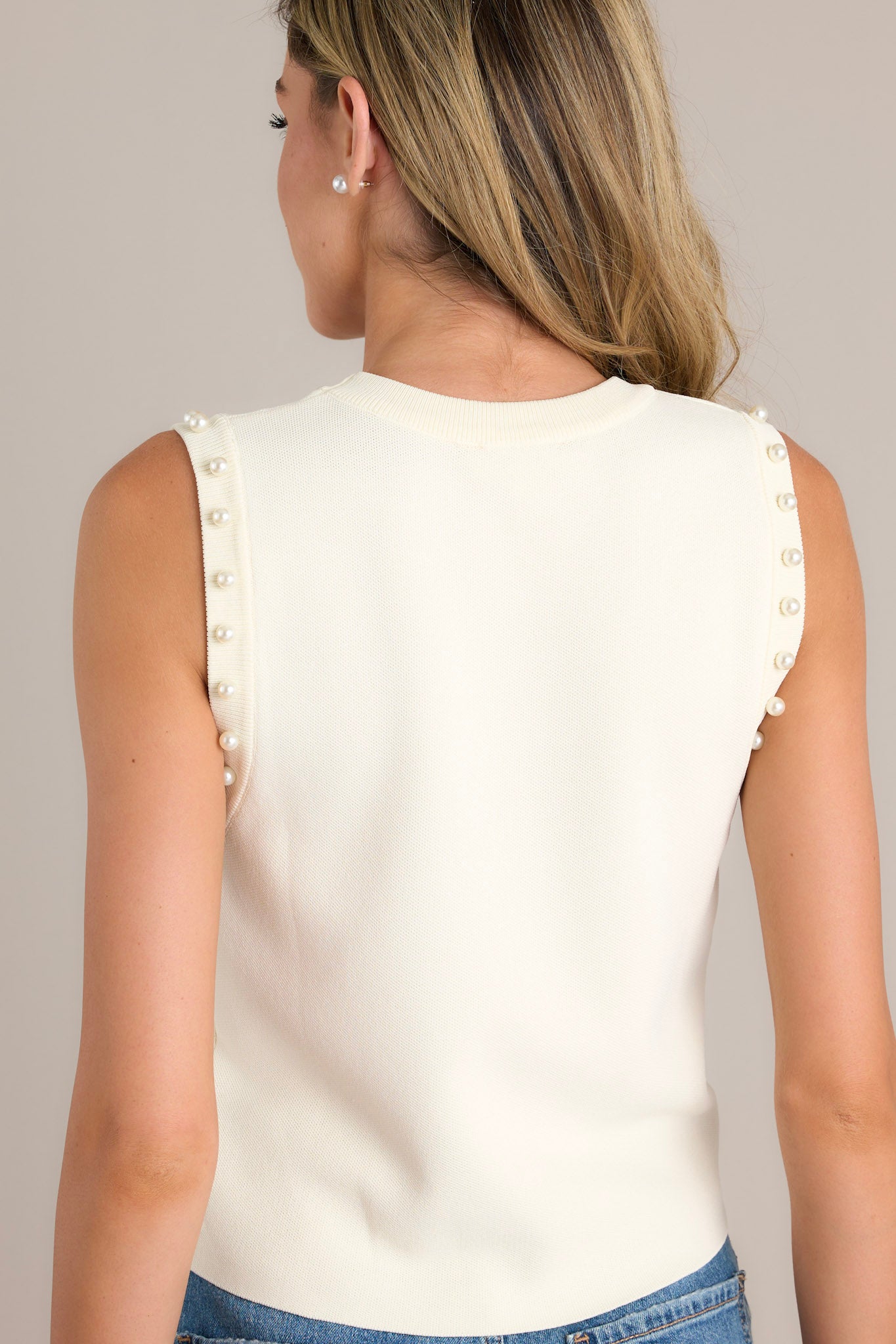 Back view of an ivory tank top showcasing the pearl embellished sleeves, soft material, and slightly cropped hemline.