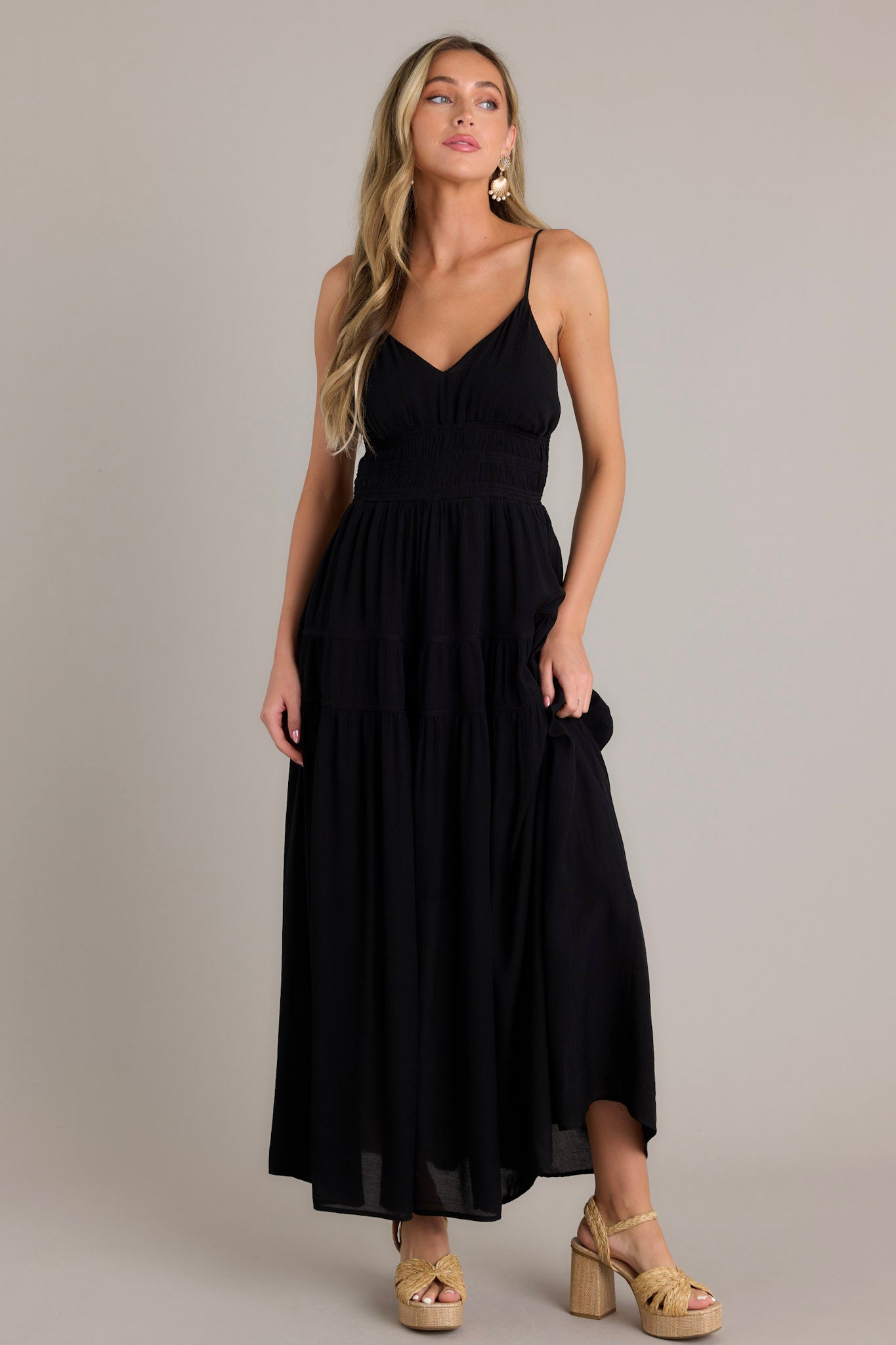 This black maxi dress features a v-neckline, thin adjustable straps, an open back, a fully smocked waist and lower back, tiers, and a flowing silhouette.