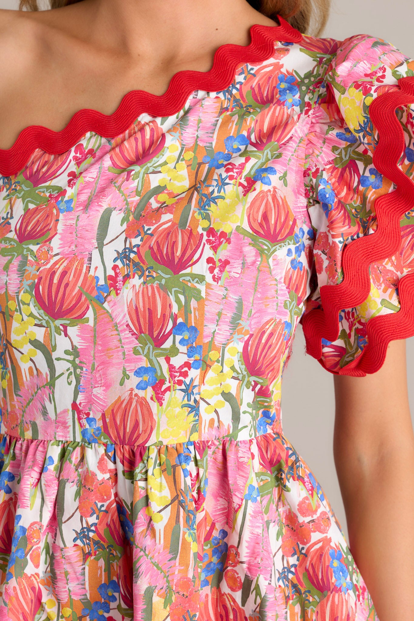 Close-up of the red multi floral romper fabric, highlighting the bold floral print and the intricate ricrac detailing.