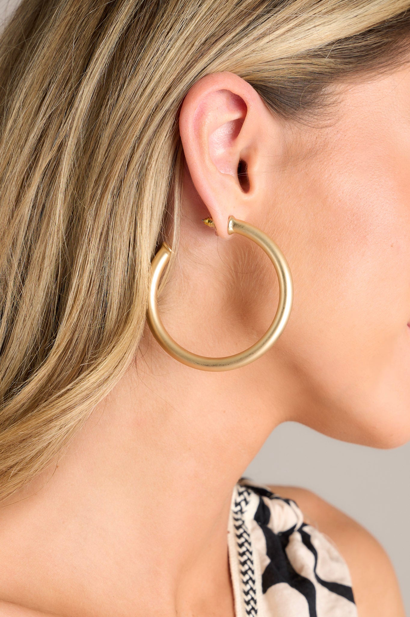 Close-up view of these matte gold earrings that feature a thick design, an incomplete hoop, and secure post backings.