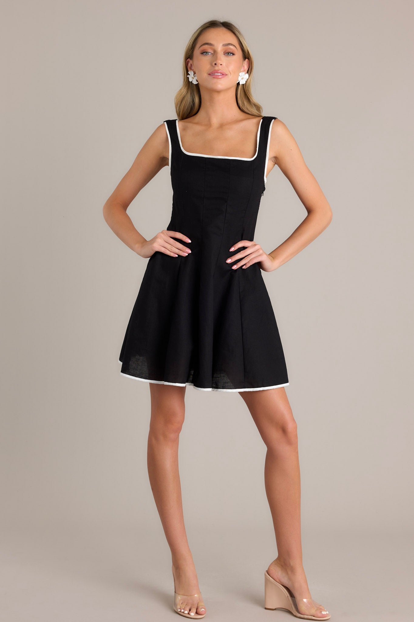 Full body shot of a black mini dress with a square neckline, thick adjustable straps, and a flattering A-line silhouette with contrasting white trim.